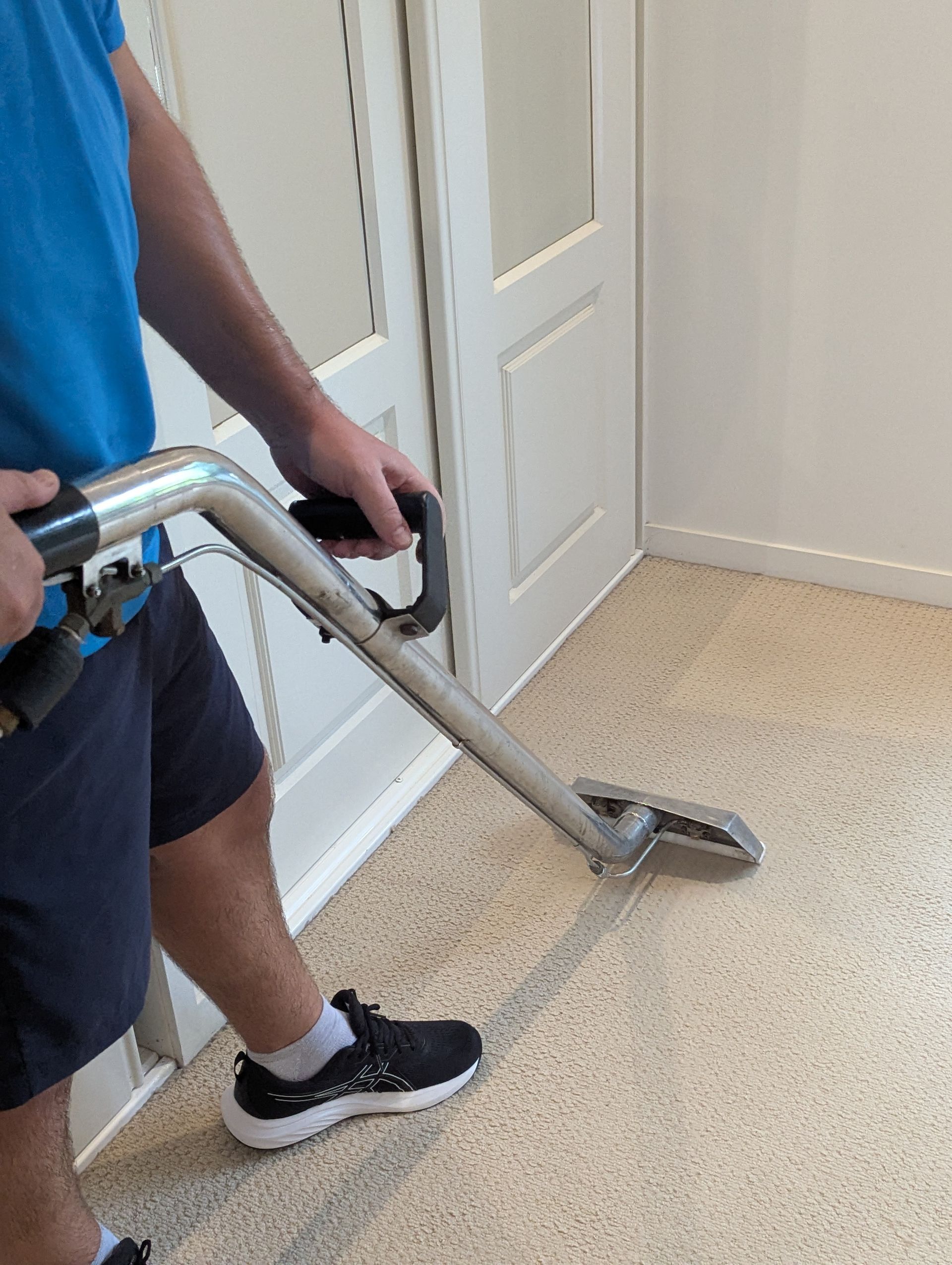 A Man Is Cleaning A Carpet With A Vacuum Cleaner— Total Pest and Carpet Cleaning in Kinka Beach, QLD