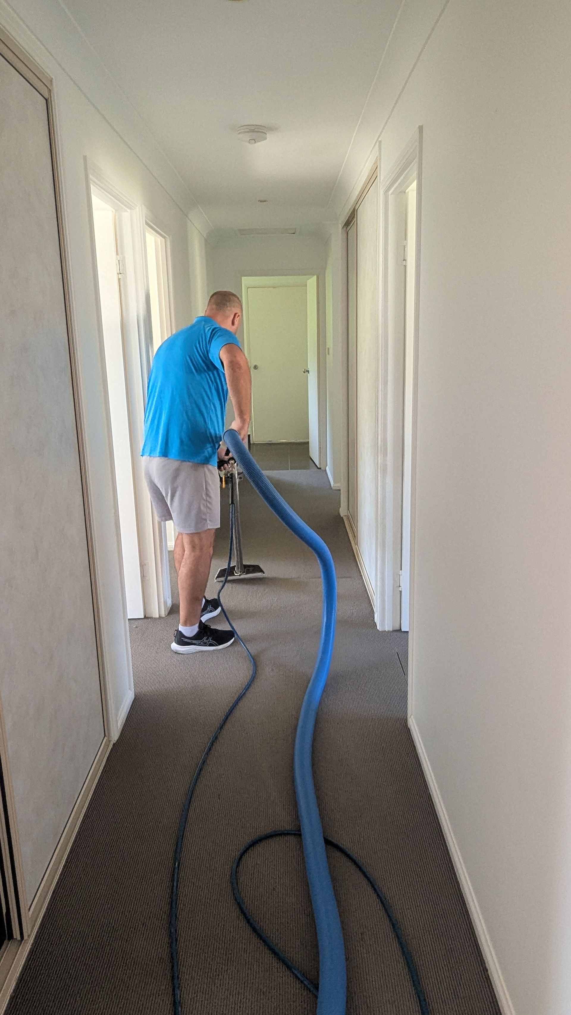 A Man is Cleaning a Carpet With a Vacuum Cleaner — Total Pest and Carpet Cleaning in Yeppoon, QLD