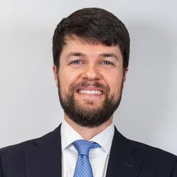 Man in suit smiles at the camera, light background.