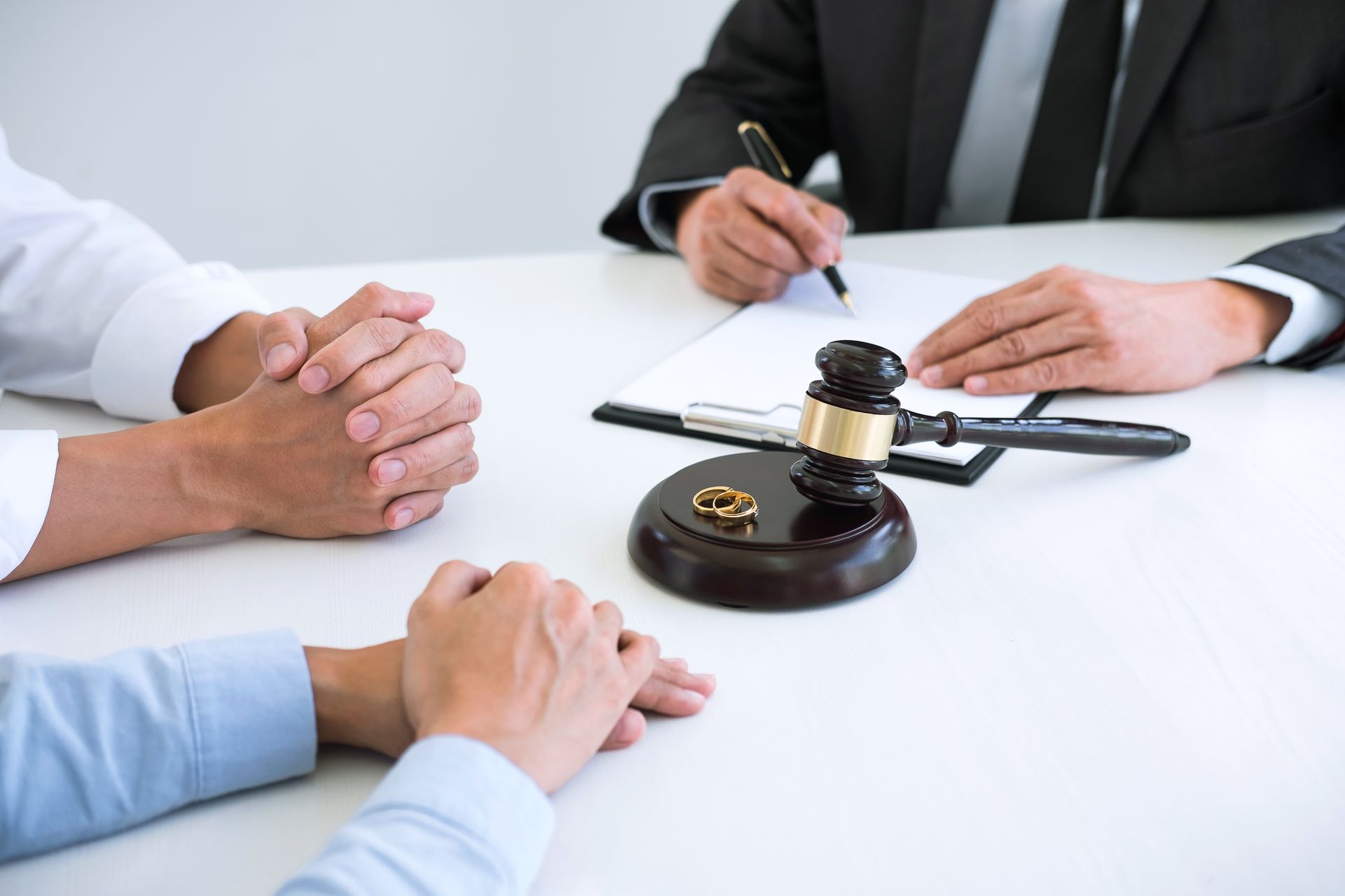 Divorce mediation: hands clasped, rings, gavel, legal documents on a table, people in suits.