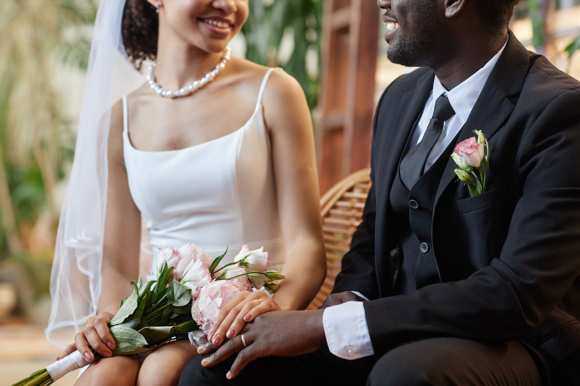 Bride and groom seated, holding hands. Bride in white dress, veil, holding bouquet. Groom in black suit, smiling.