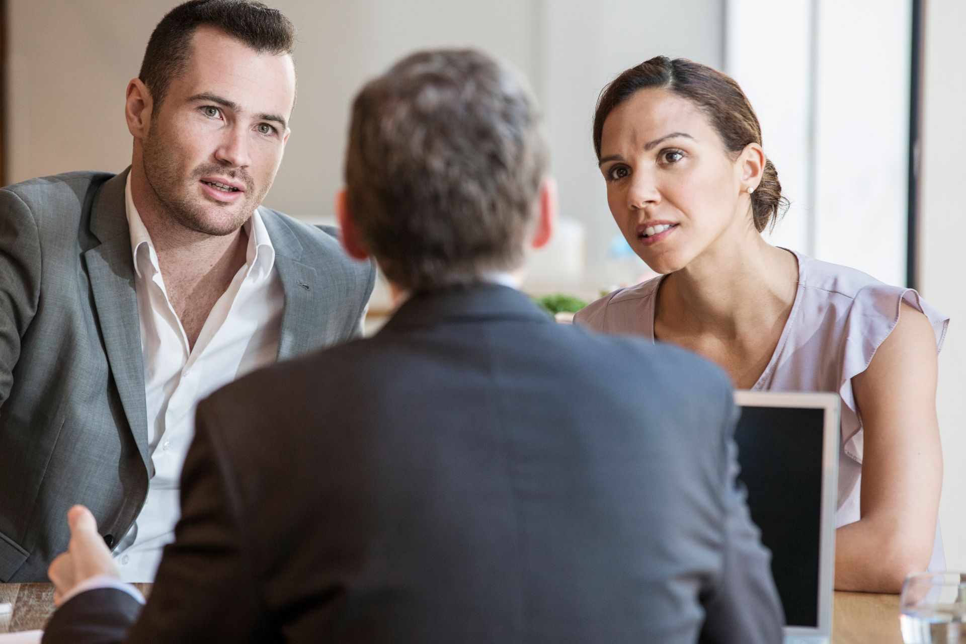 Couple talking with a person in a suit, possibly a meeting, indoors.