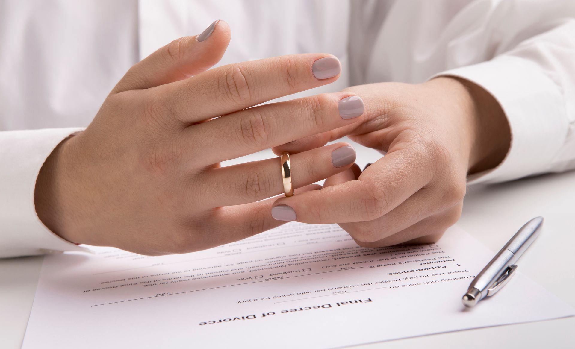 Person removing wedding ring, divorce papers and pen on table.