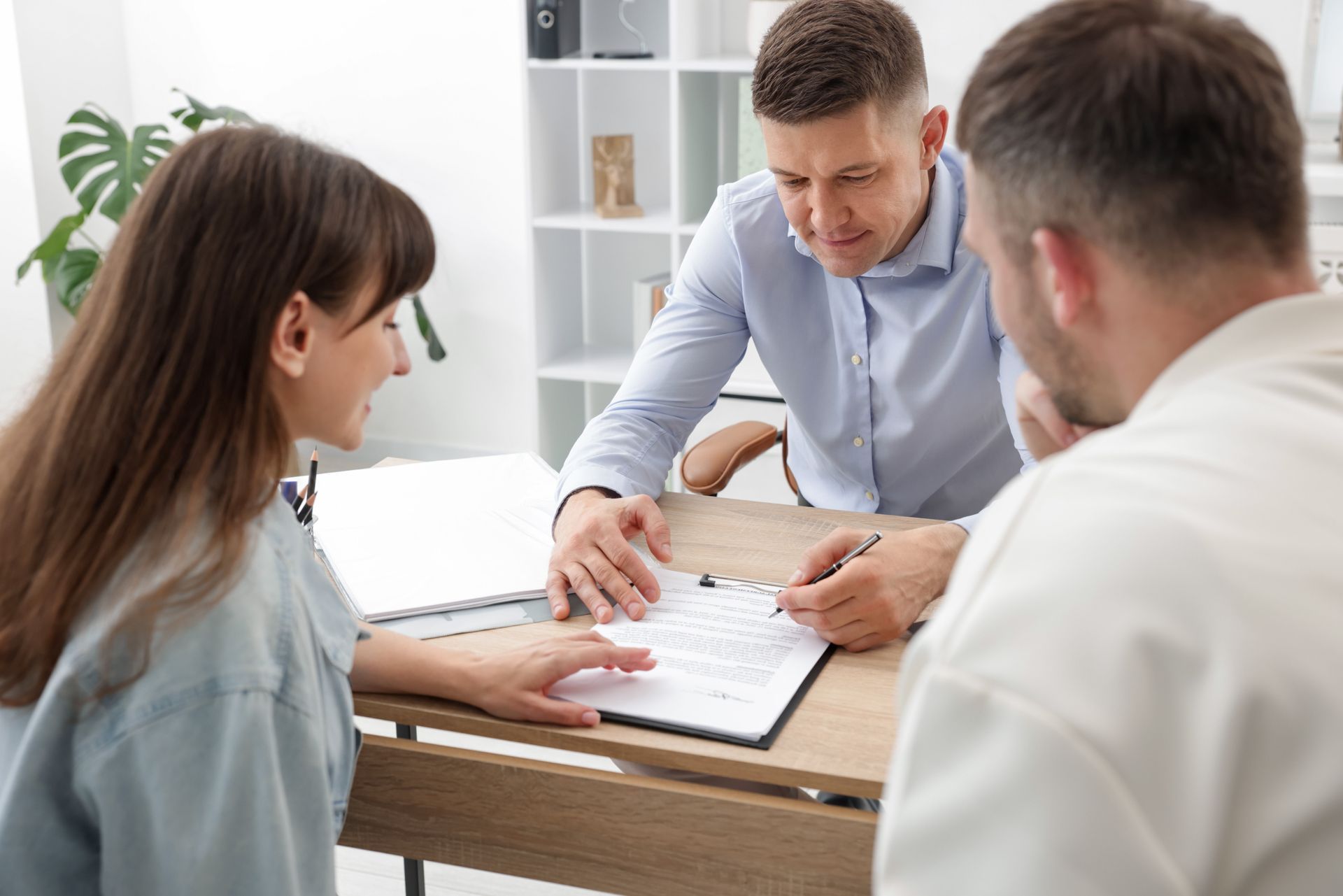 Couple signing documents at a table with an advisor in an office setting.