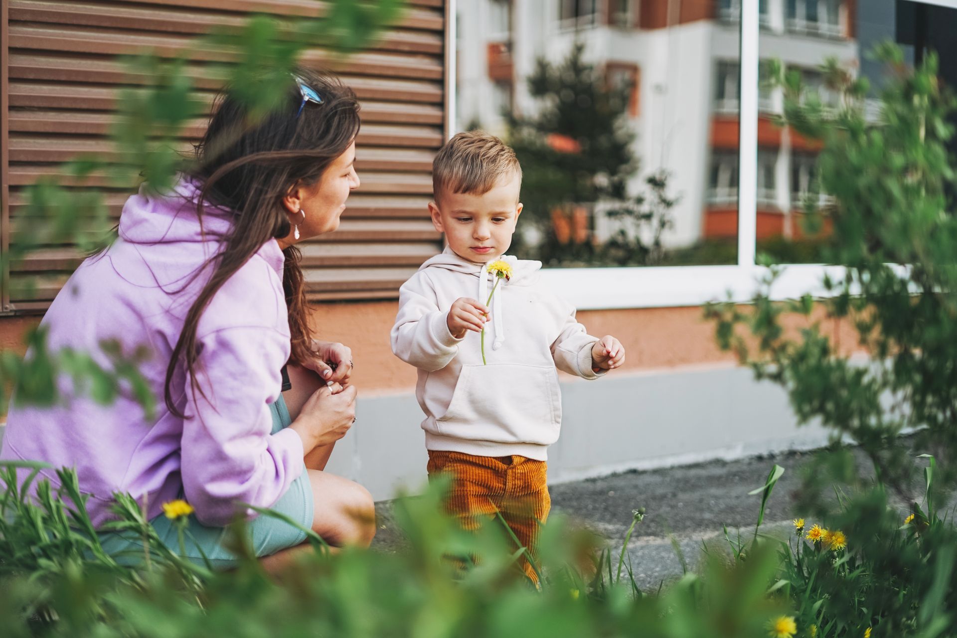 Woman and child looking at a dandelion in a garden. The child is holding the flower. Exterior shot.