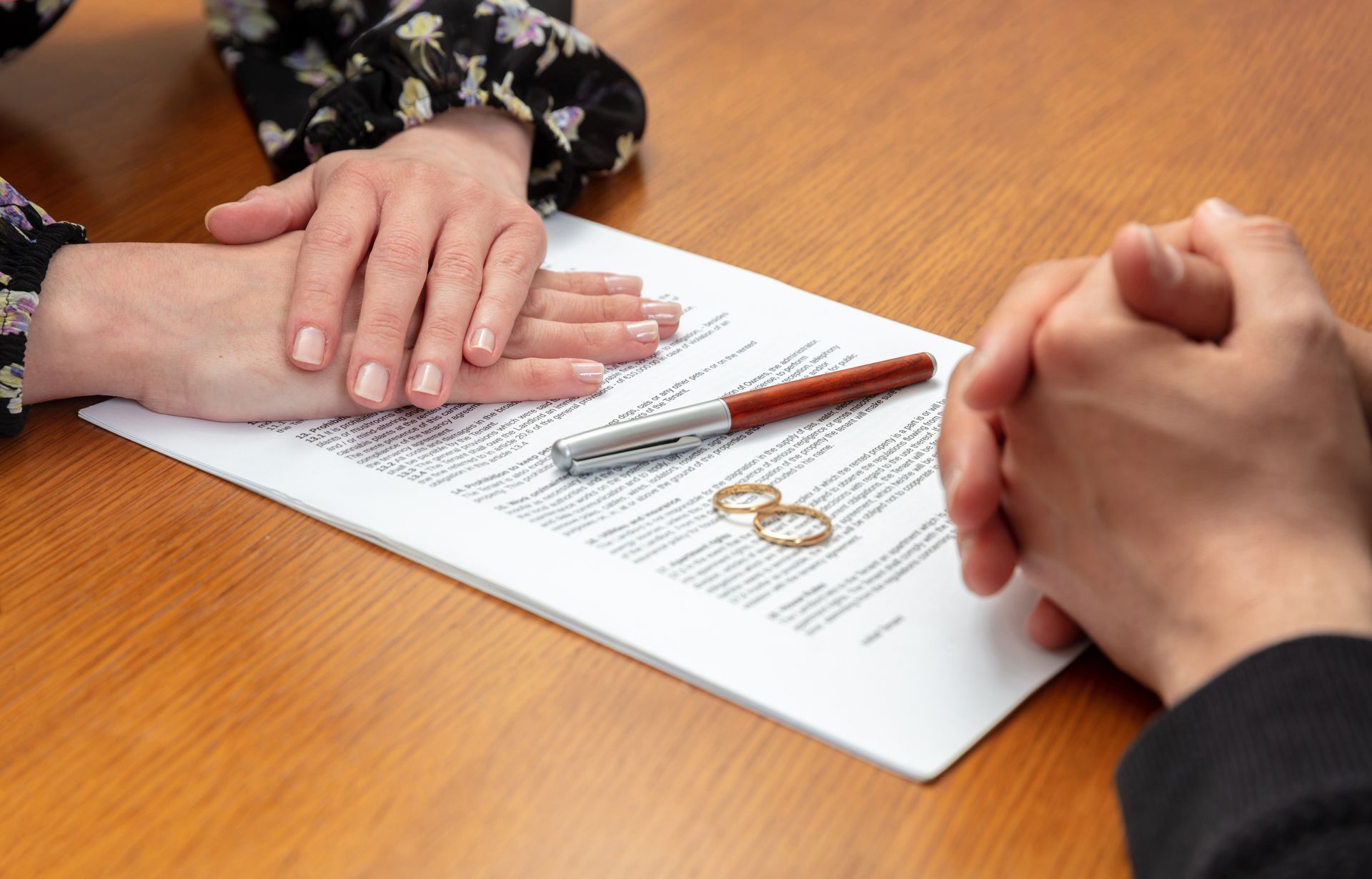 Hands resting on a divorce agreement with rings and a pen on a table.