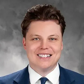Man in a blue suit smiles, looking at the camera against a neutral background.