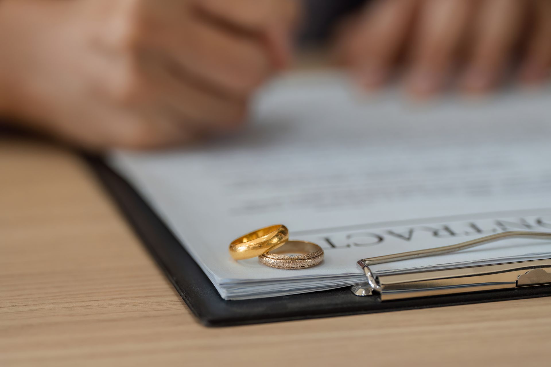 Wedding rings on a divorce document as a person signs it with a pen.