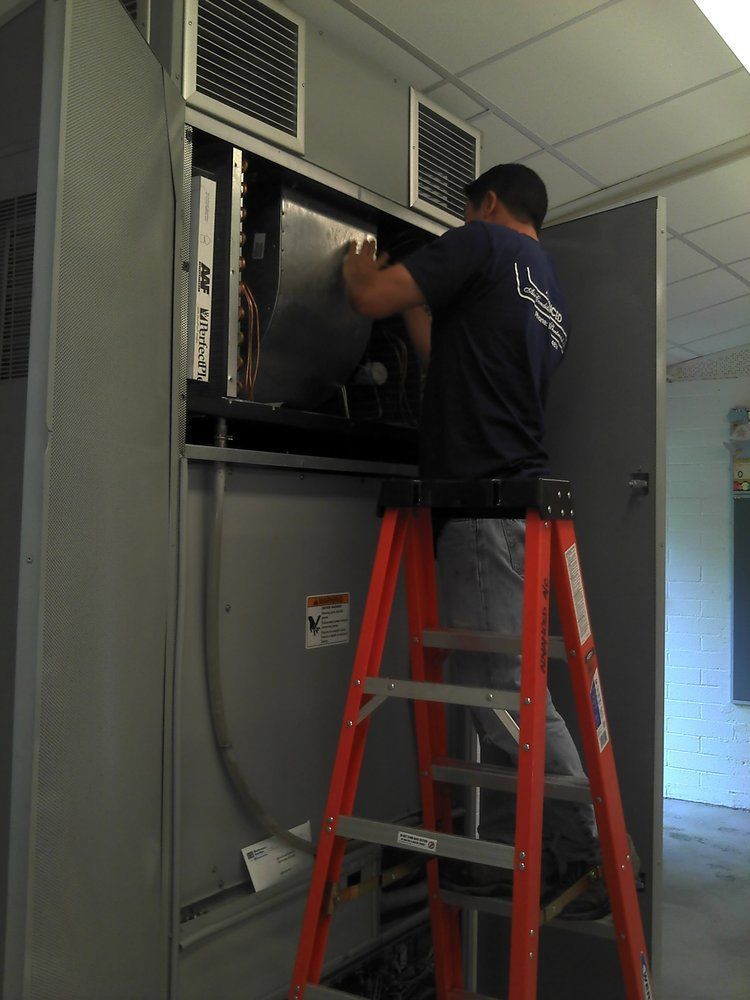 A man standing on a ladder working on a electrical box.