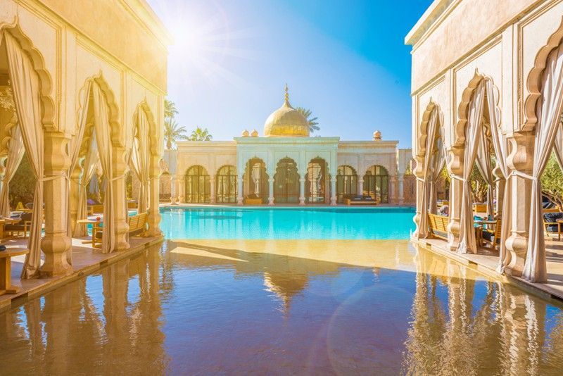 A luxurious resort with a golden dome, reflecting in a large pool. Sunlit arches frame the scene, evoking serenity.