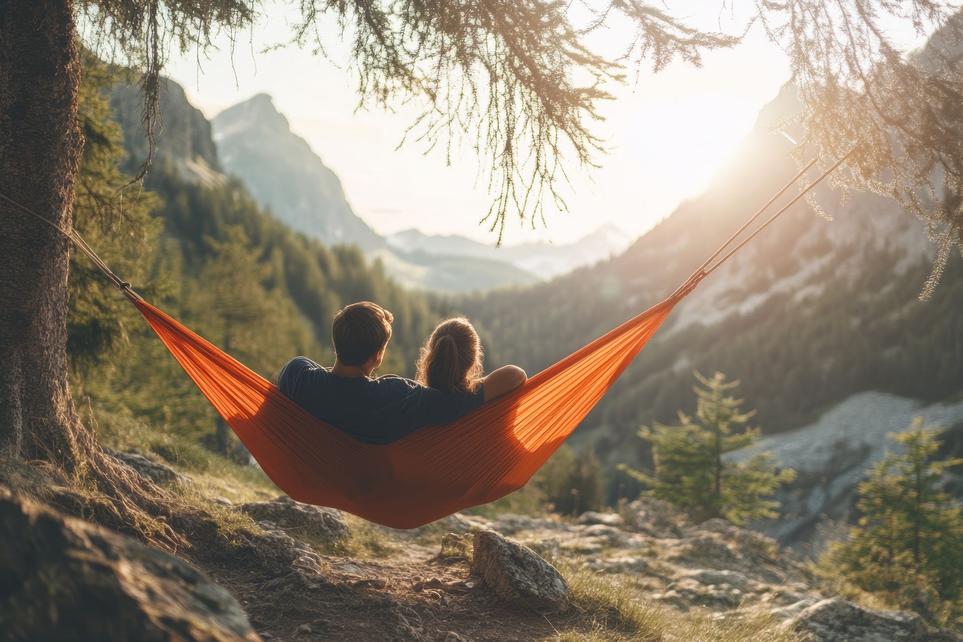 Couple in orange hammock, backs to camera, enjoying a mountain view at sunset.
