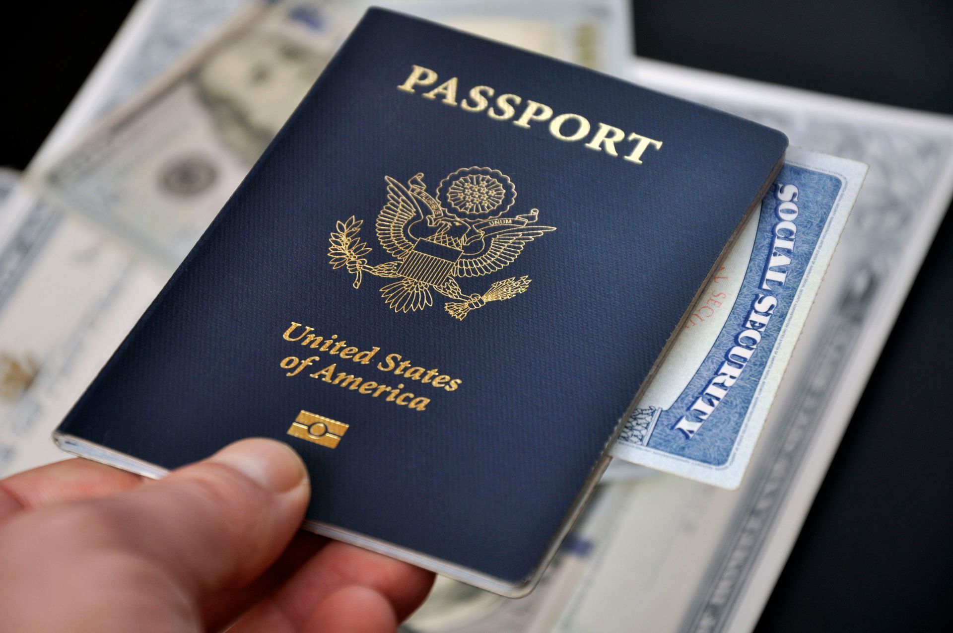 Person holding a U.S. passport with a Social Security card peeking out; resting on currency.