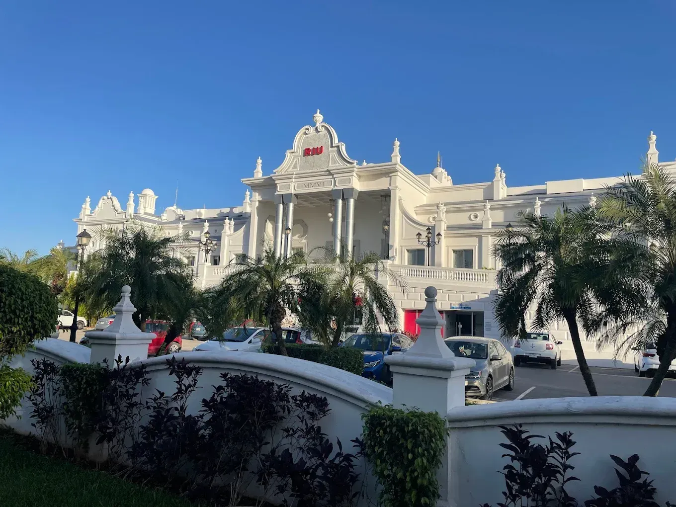 White ornate building with palm trees, cars, and a blue sky. The sign on the building says 
