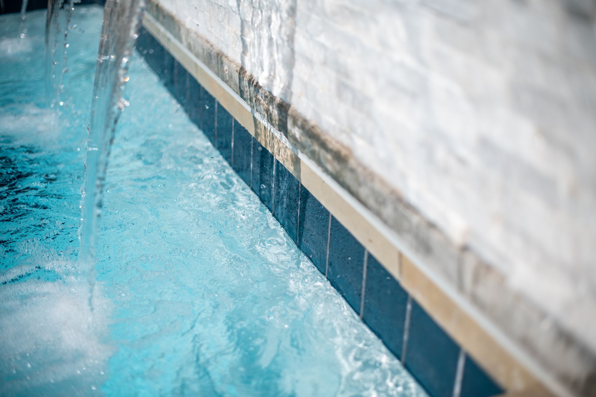 Water cascades from a stone wall into a blue-tiled swimming pool.
