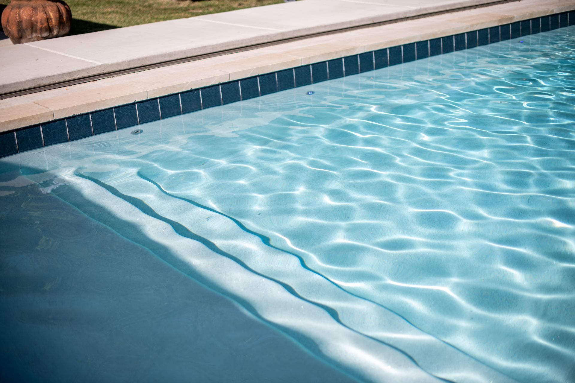 A light blue swimming pool with steps leading into the water, bordered by a beige concrete deck.