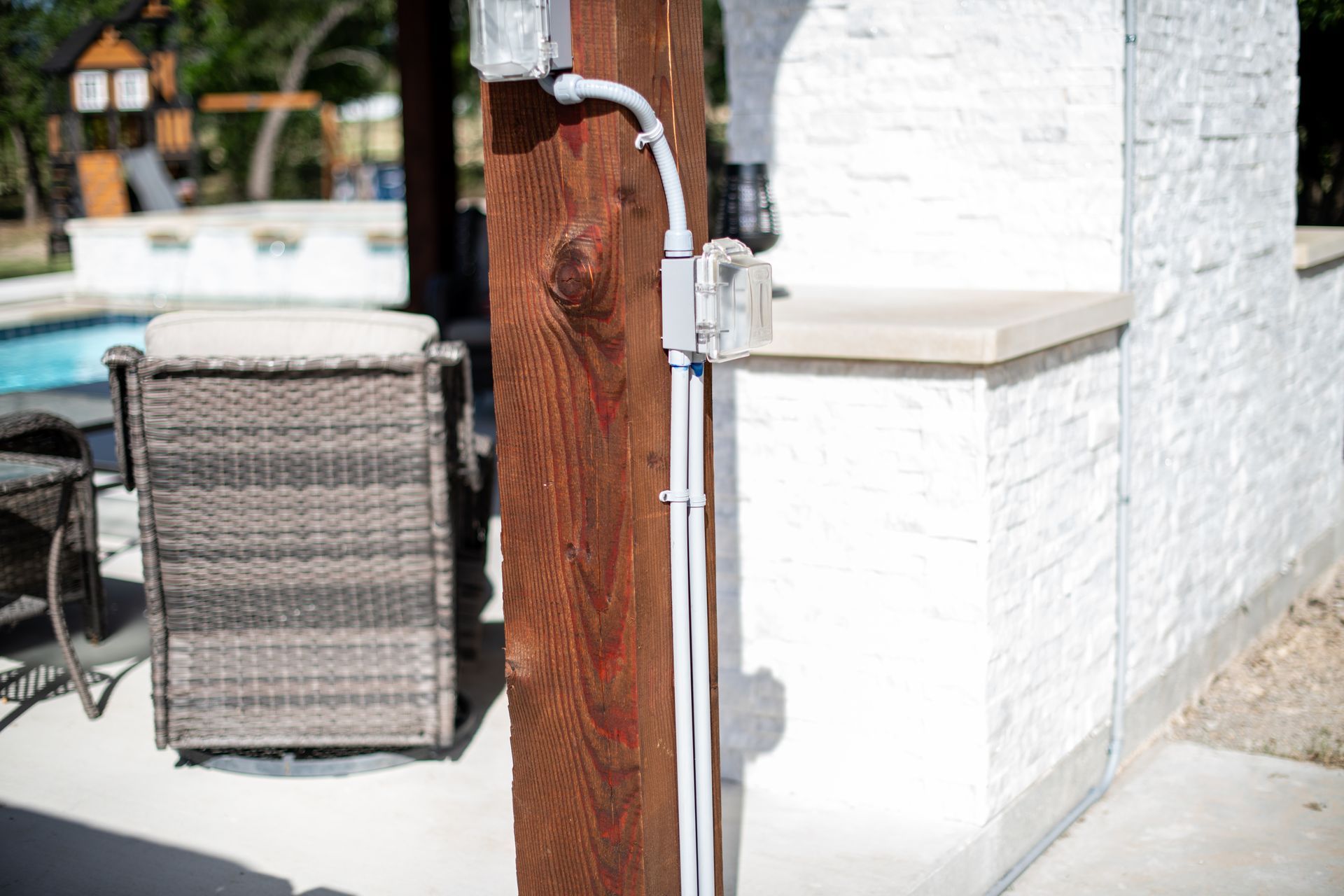 Electrical conduit and boxes mounted on a wooden post beside an outdoor patio area.