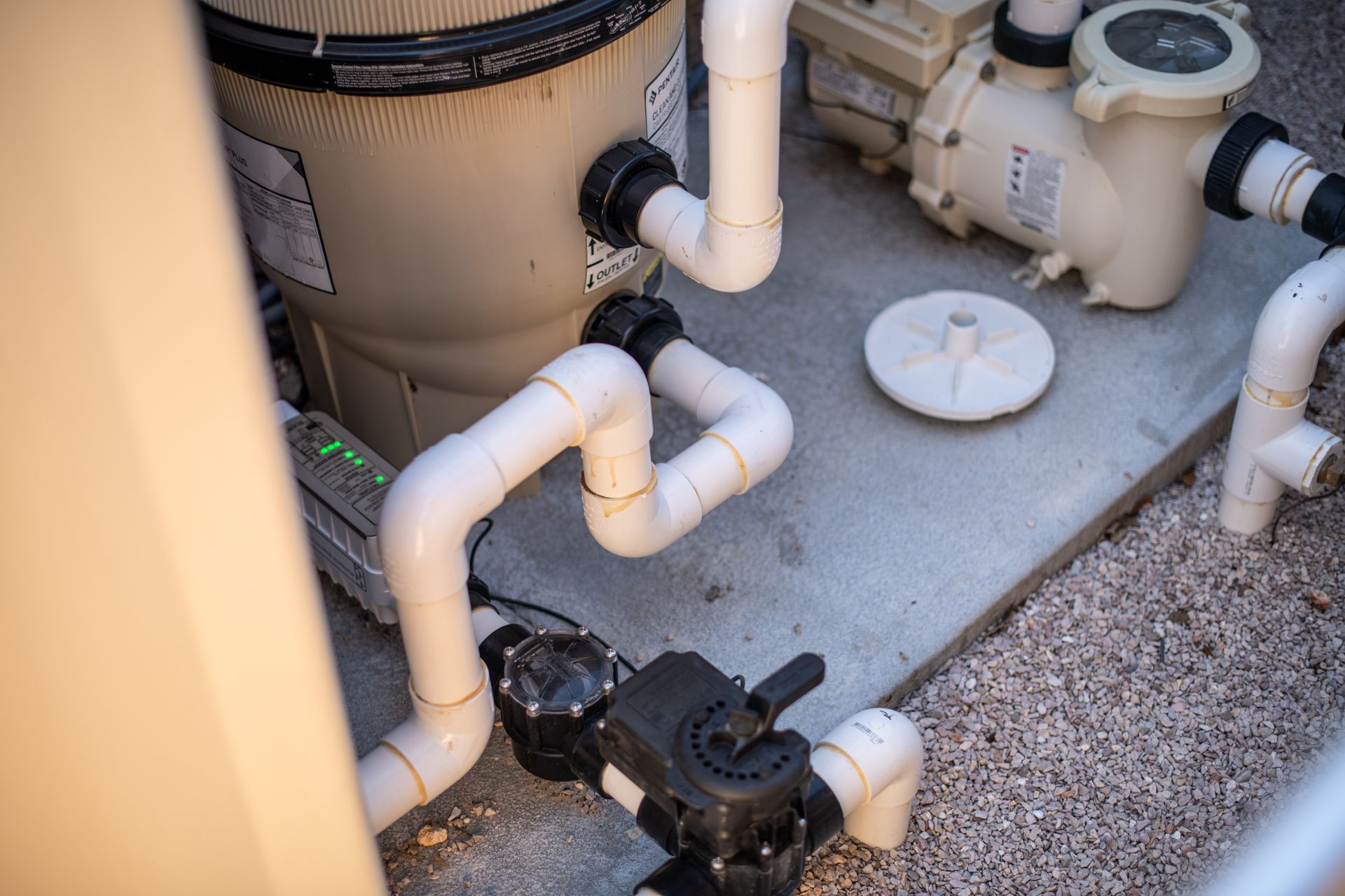 Pool equipment setup with a beige filter tank, white PVC pipes, and a black valve on a concrete pad.