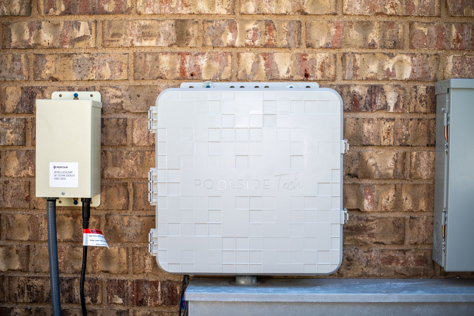 Three utility boxes mounted on a brick wall, with a large, square light gray telecommunications box in the center.