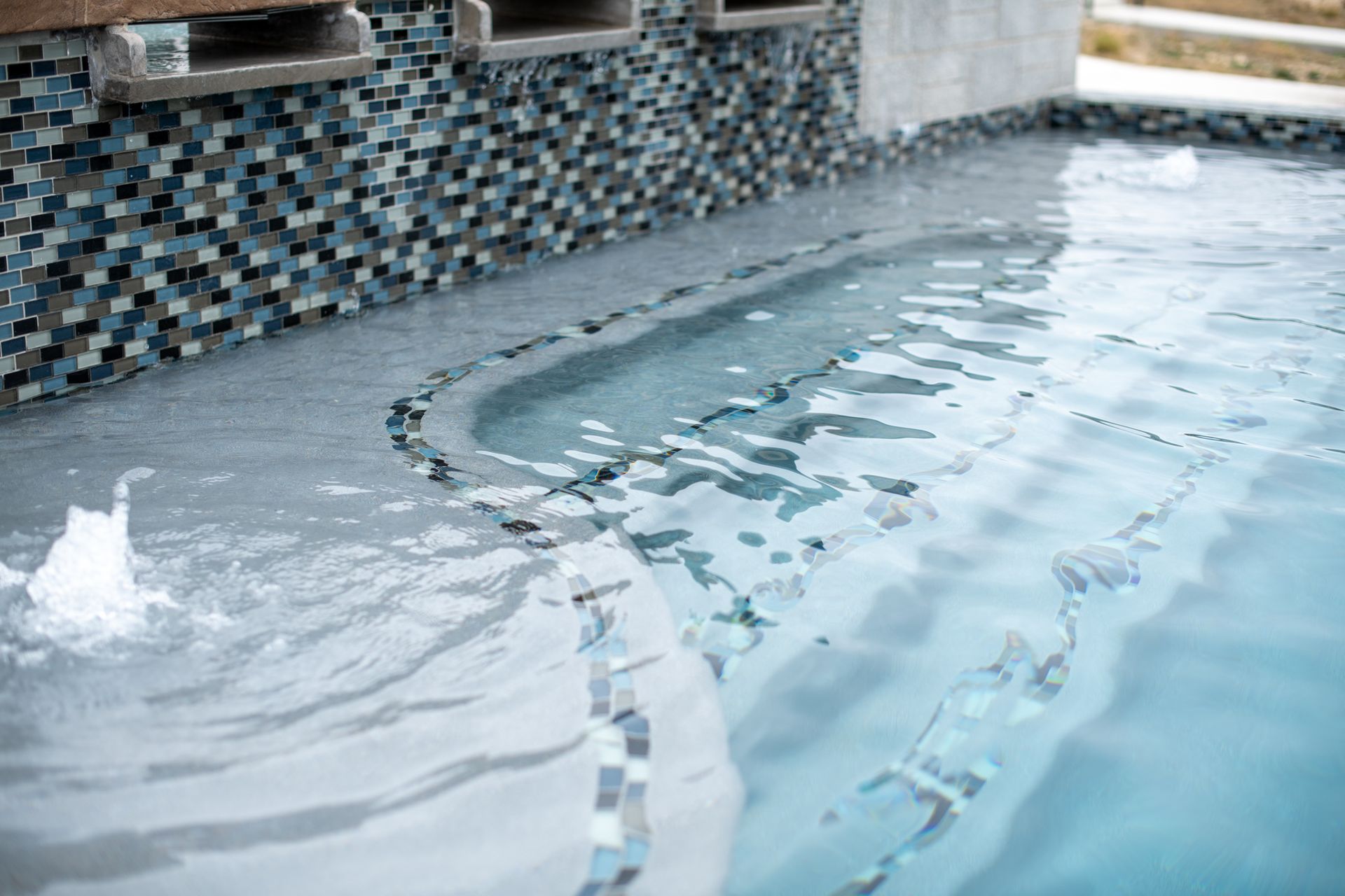 A pool featuring a tiled wall, water feature, and shallow steps leading into clear blue water.