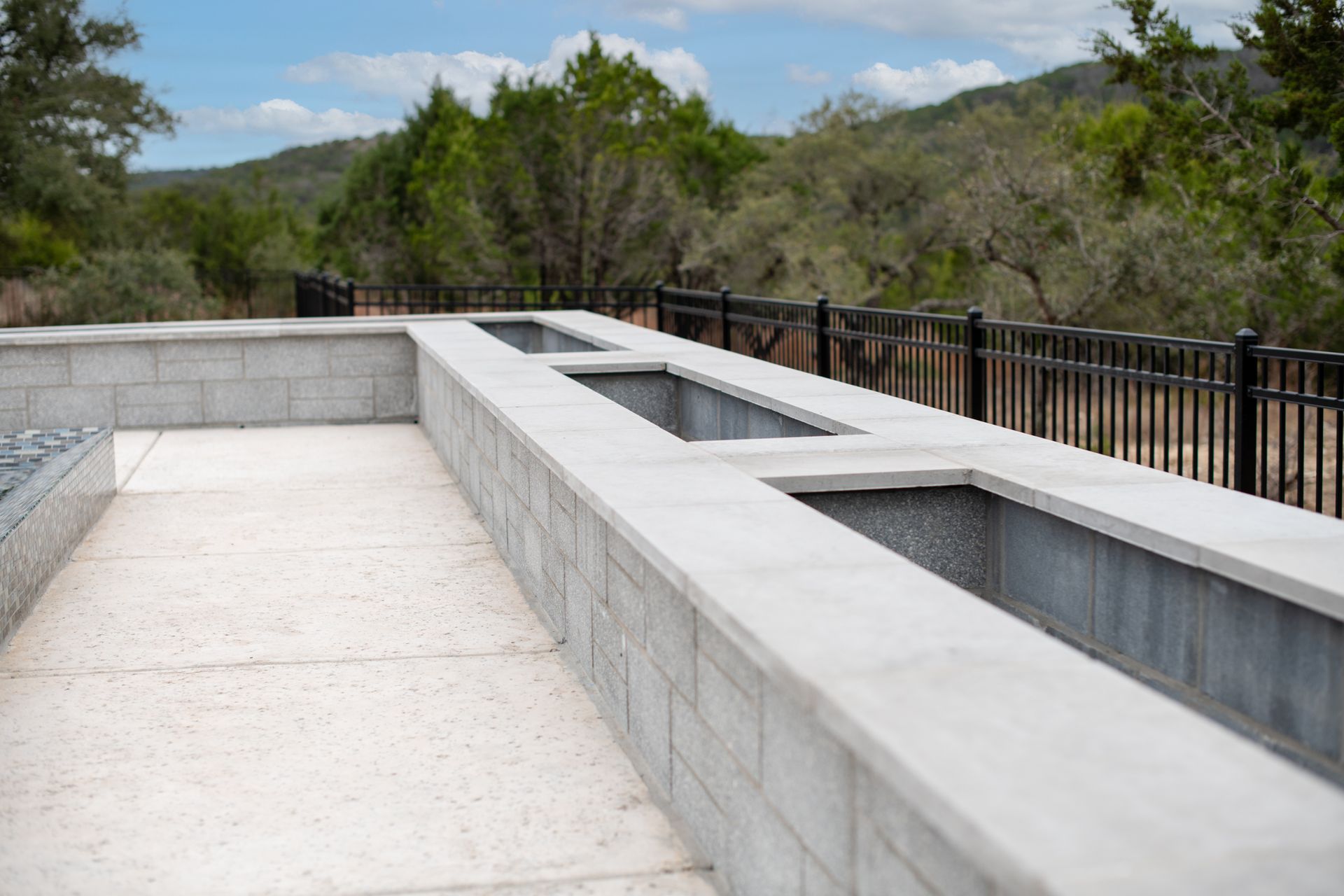 A long, light-gray concrete outdoor counter with built-in troughs, set on a patio overlooking a forested hillside.