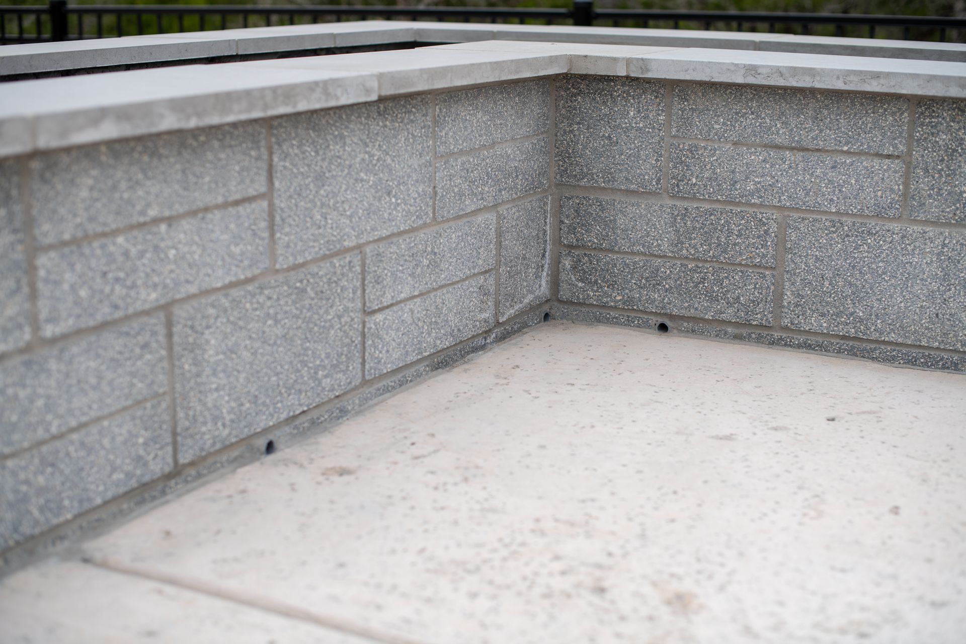 A corner section of a light gray concrete block wall with a smooth cap, built upon a light concrete base.