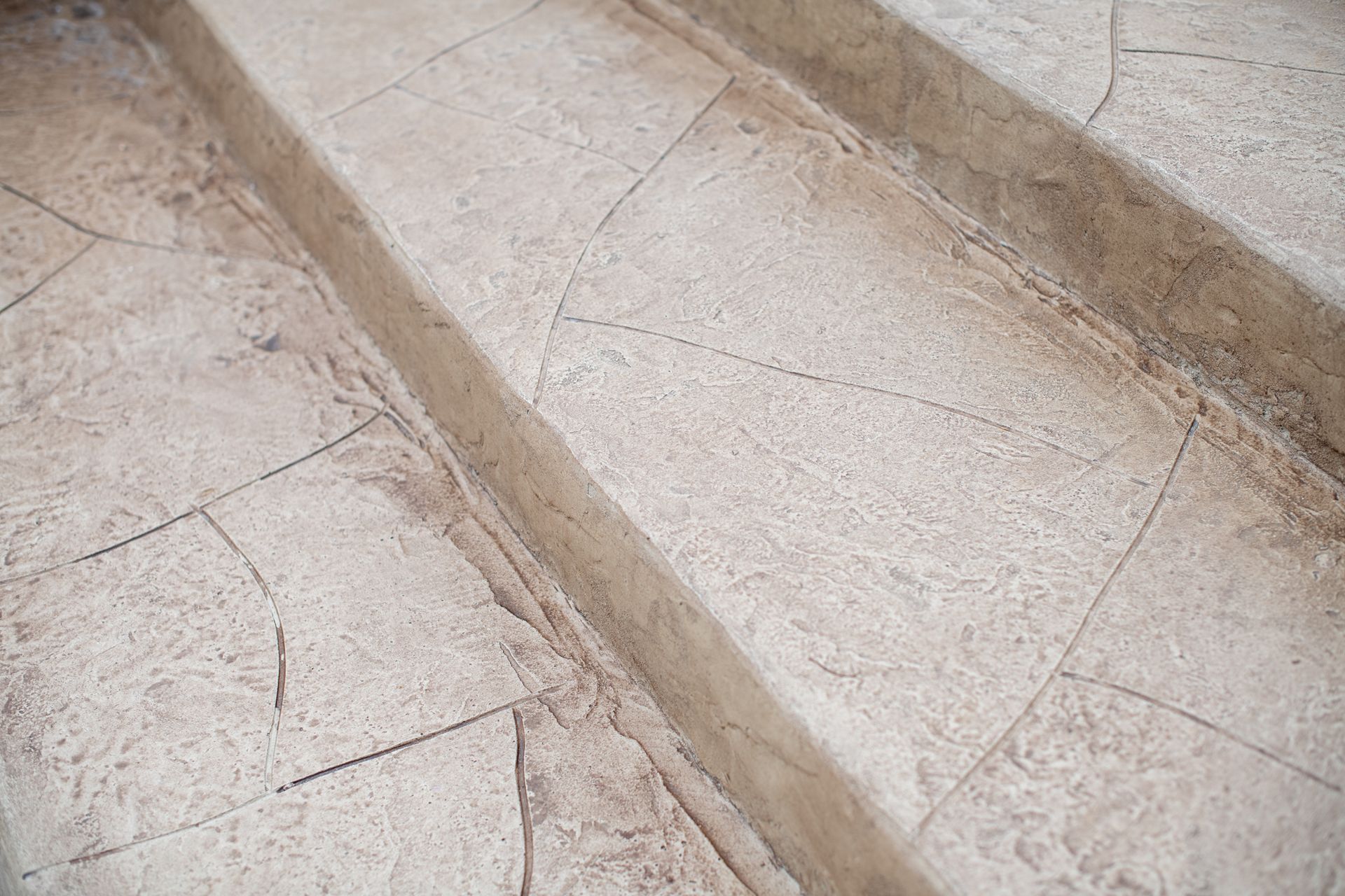 A close-up view of stone steps with a light, textured finish and diagonal crack patterns.