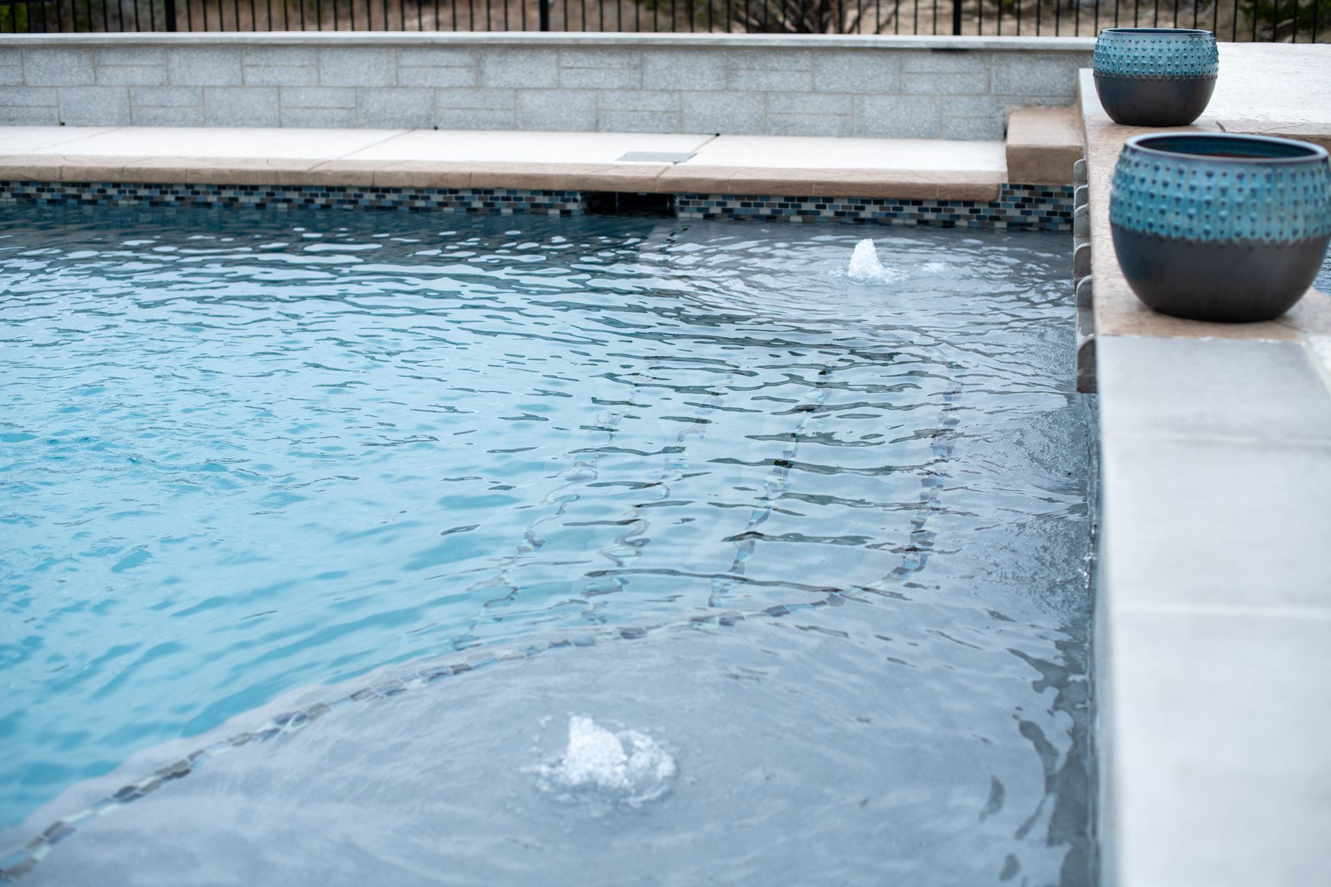 A swimming pool features a shallow ledge with two water fountains and two decorative teal bowls on the pool deck.