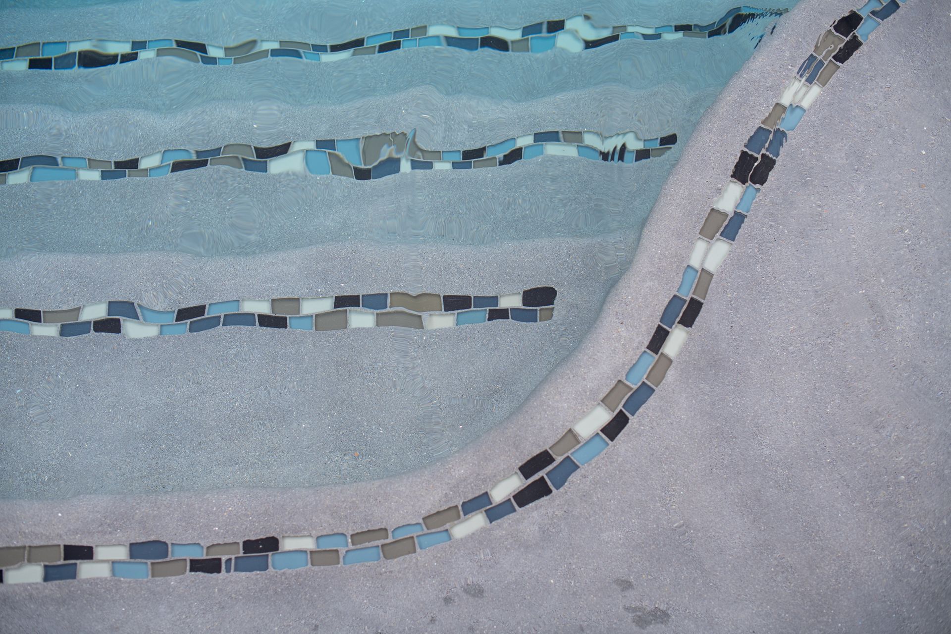 A high-angle view of pool steps featuring horizontal safety tile markers in shades of blue, gray, and white.