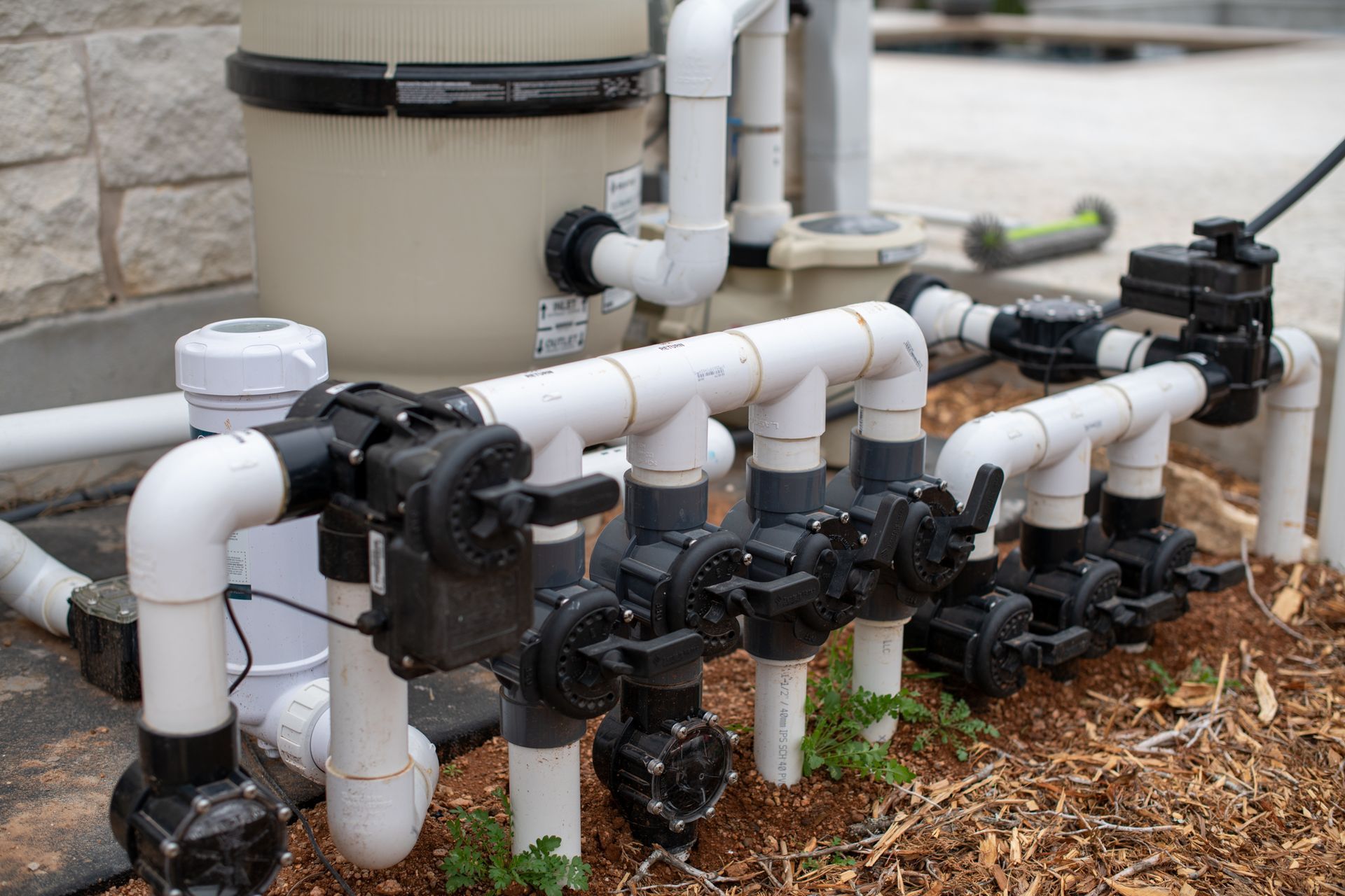 A pool equipment setup featuring a large filter tank and a row of PVC pipes with several black control valves.