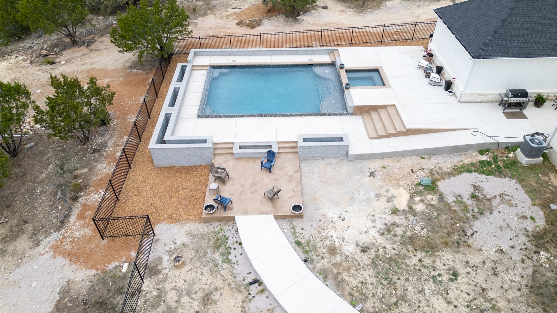An aerial view of a backyard featuring a rectangular swimming pool, adjacent hot tub, concrete patio, and seating area.