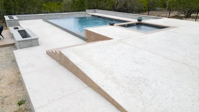 A modern swimming pool and spa area with a stone patio, fire pits, and integrated stairs leading to the deck.