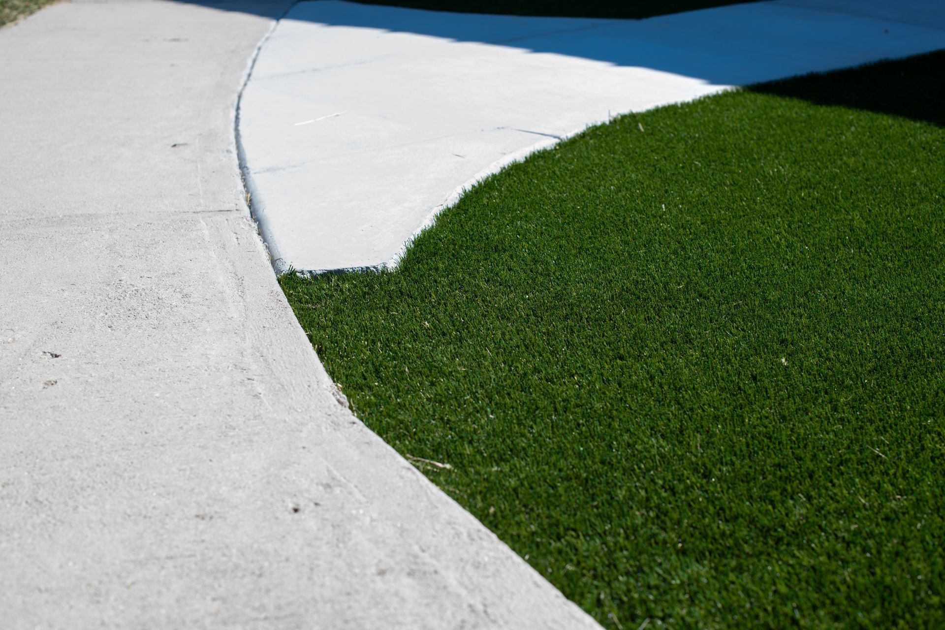 A curved concrete walkway borders a lush green artificial grass lawn under bright sunlight.