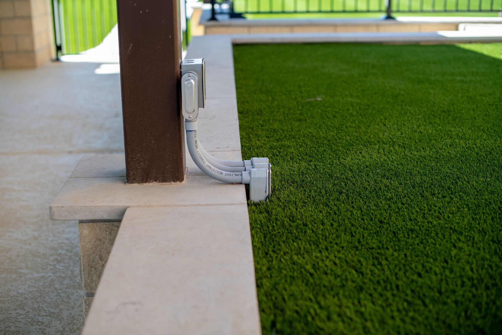 An outdoor electrical outlet mounted on a wooden post with flexible conduit connecting to a box at the grass edge.