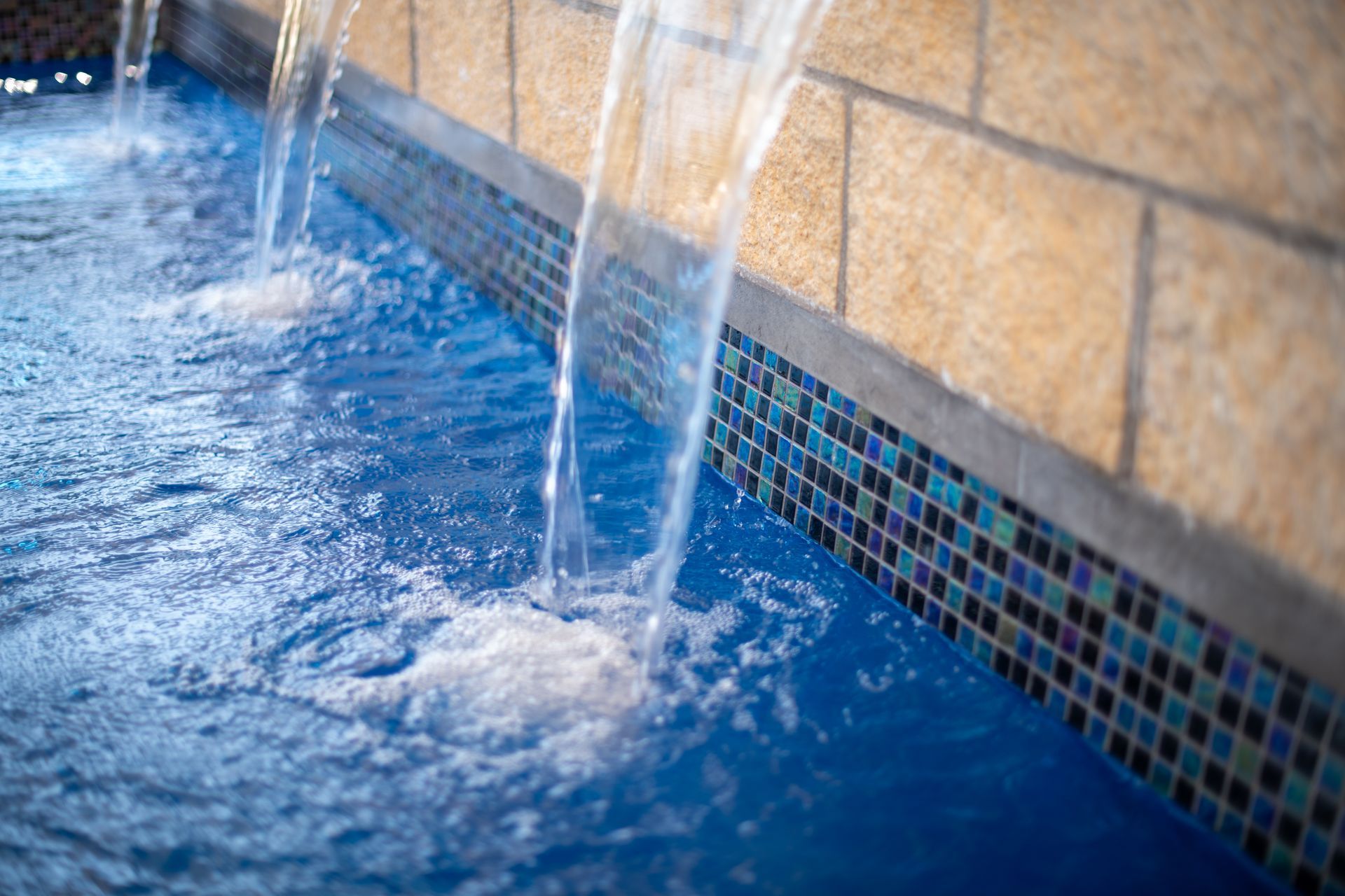 Water streams fall from a stone wall into a blue pool decorated with colorful mosaic tiles.