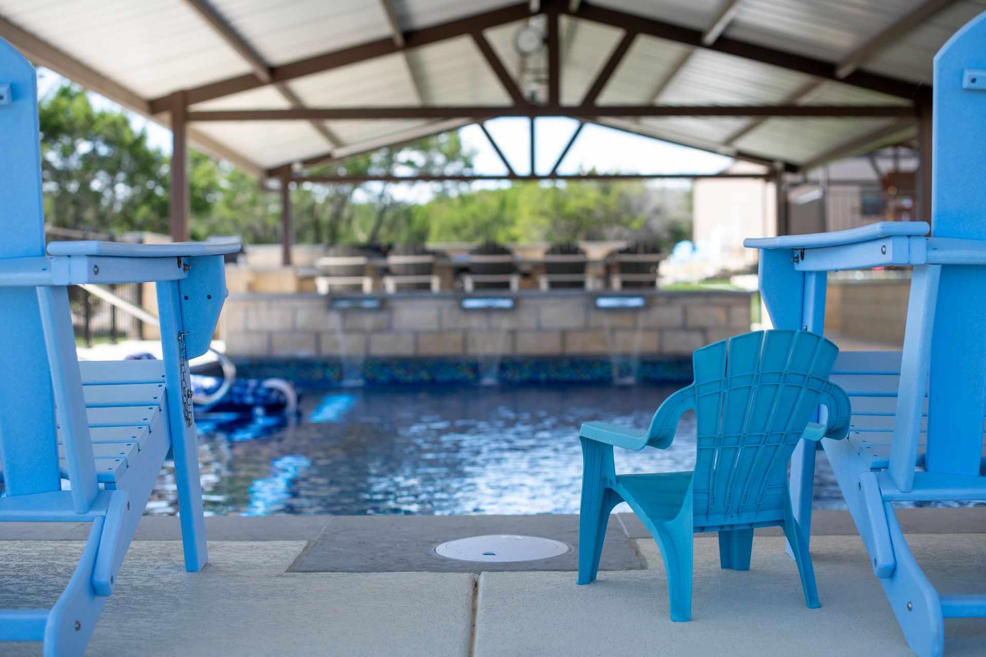 Three bright blue chairs, including one child-sized chair, face a pool under a covered patio.