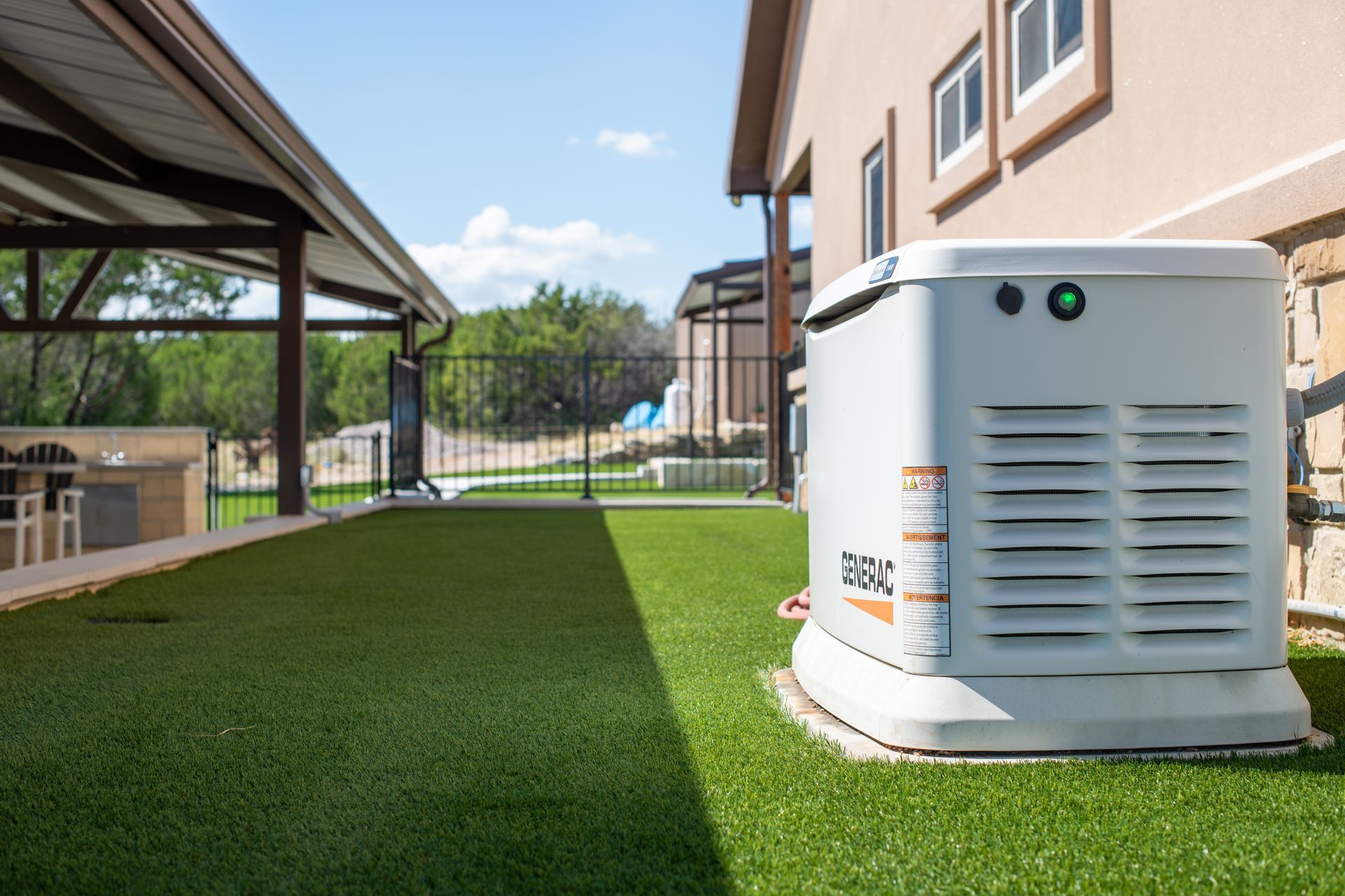 A white Generac standby generator sits on a stone base on a patch of artificial turf next to a house.