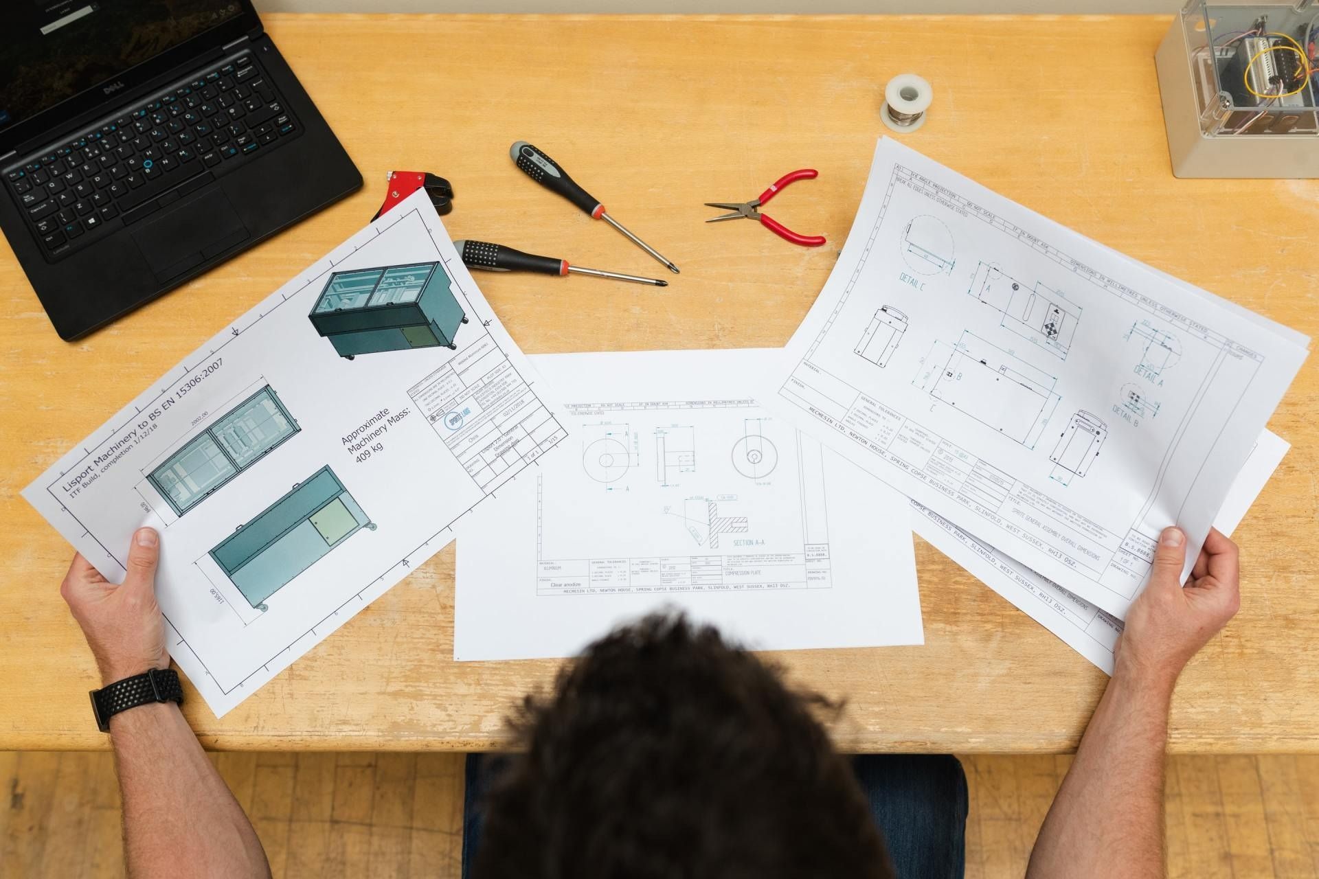 A man is sitting at a desk looking at drawings and a laptop.