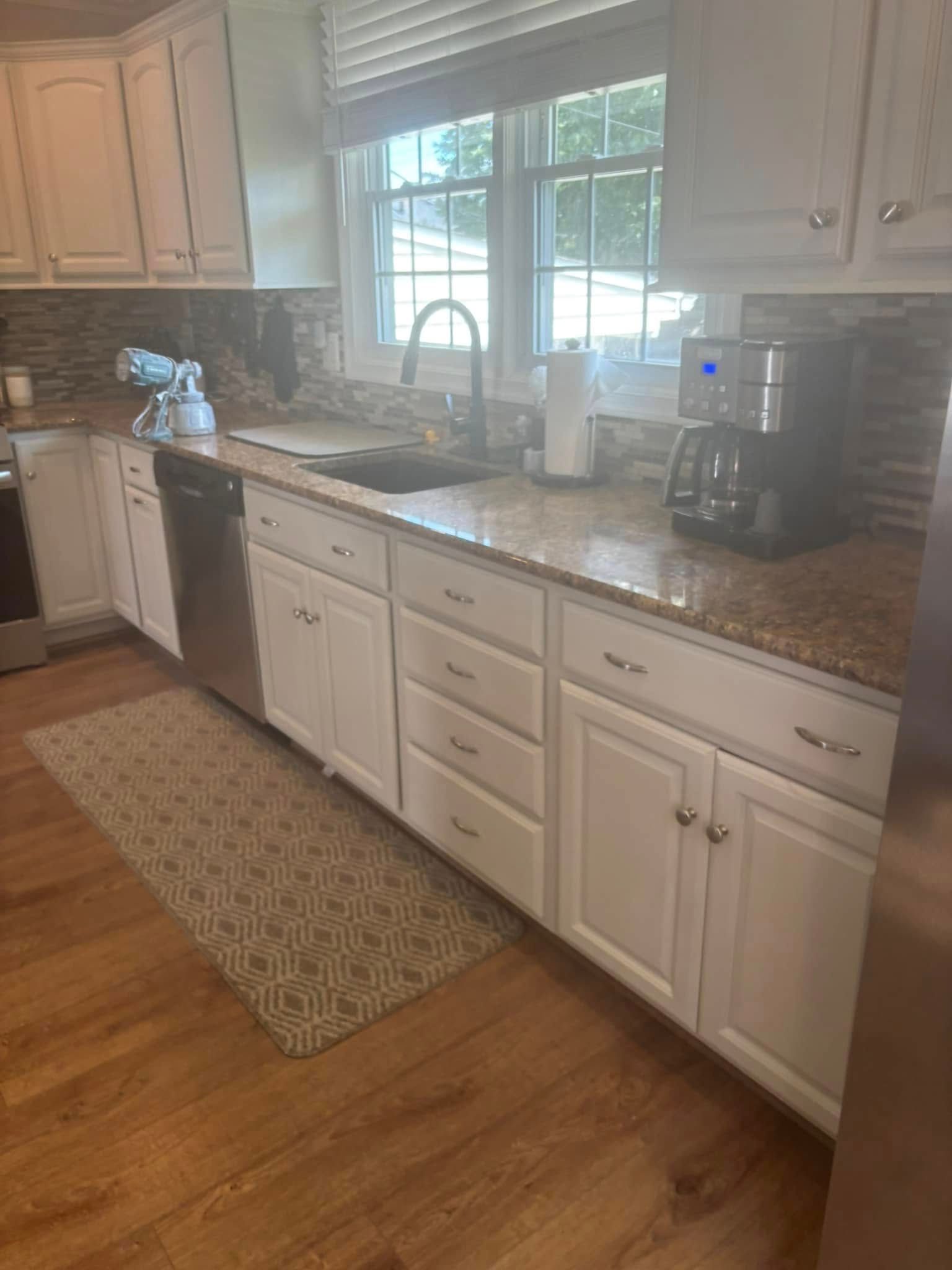 A kitchen with white cabinets , granite counter tops , stainless steel appliances , and hardwood floors.