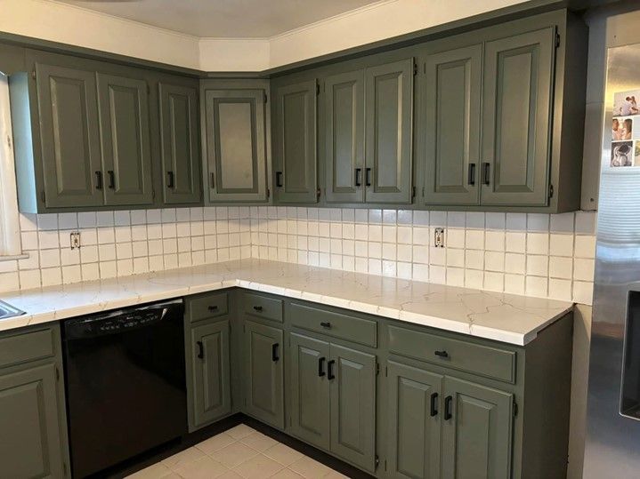 A kitchen with green cabinets and white counter tops.