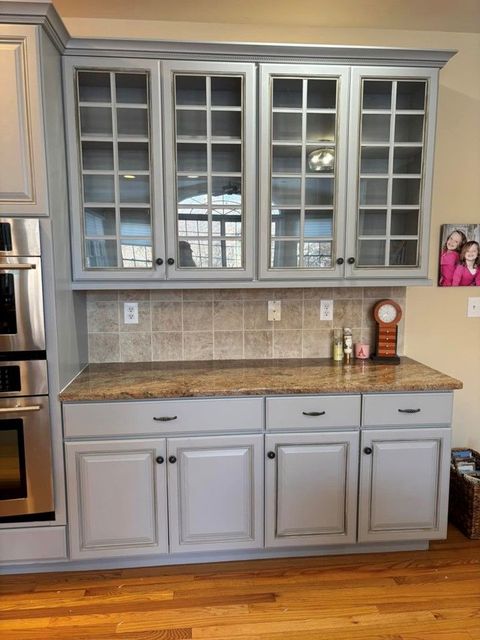 A kitchen with gray cabinets , granite counter tops , and stainless steel appliances.