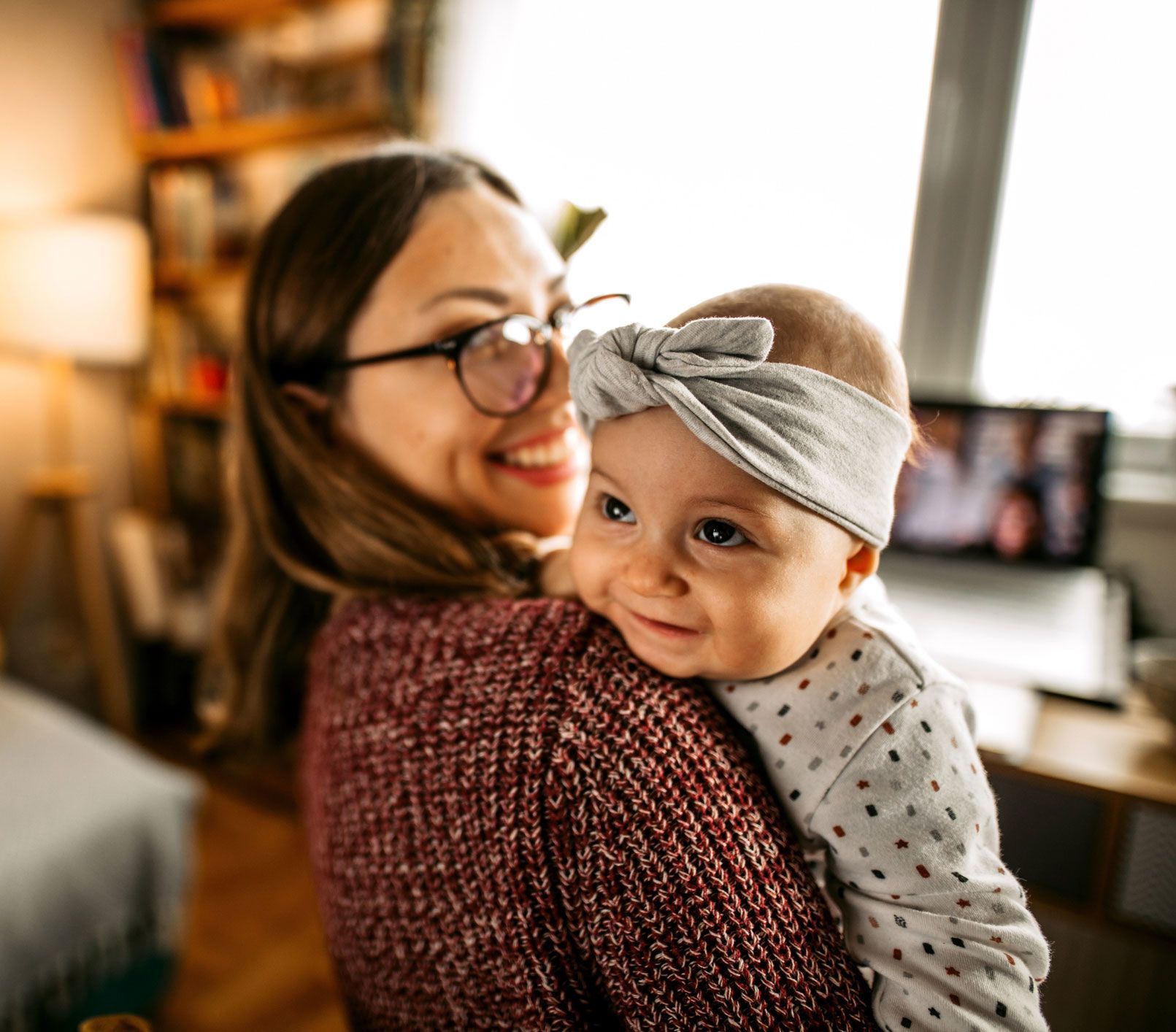 A woman wearing glasses is holding a baby in her arms.