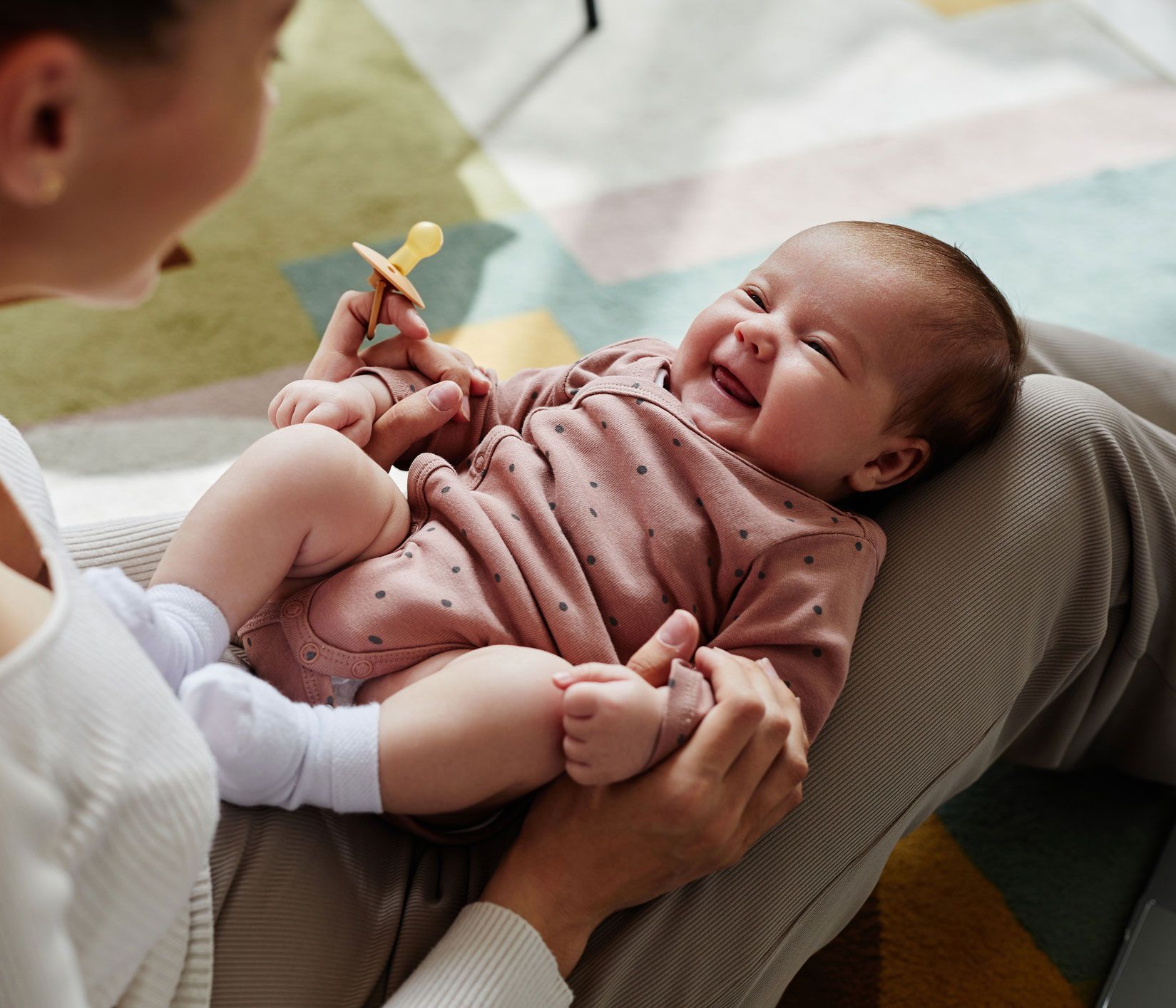 A woman is holding a baby with a pacifier in her hand.