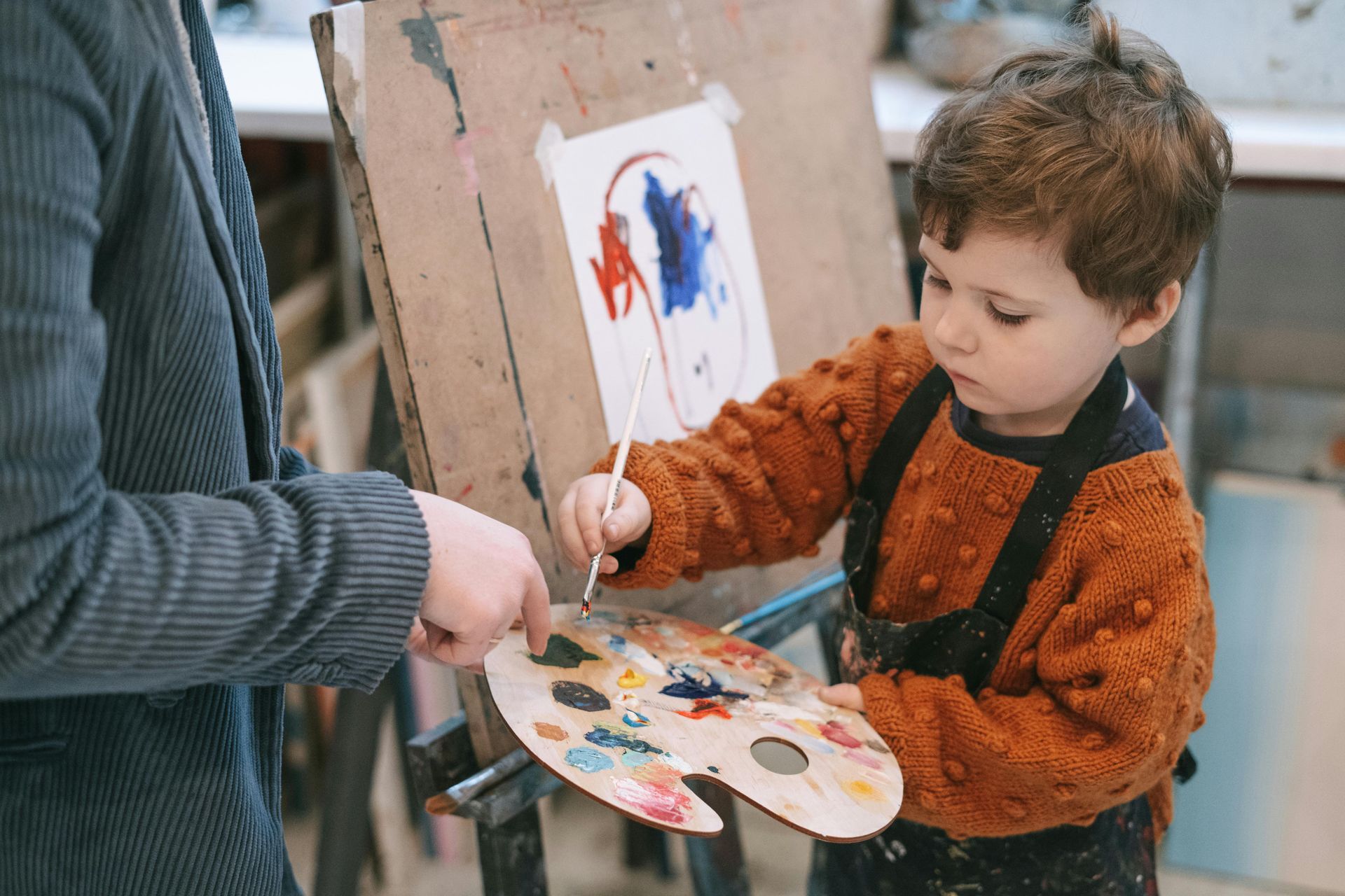 A little boy is painting a picture with a brush on an easel at Kids Creation Stations in Tampa, FL.
