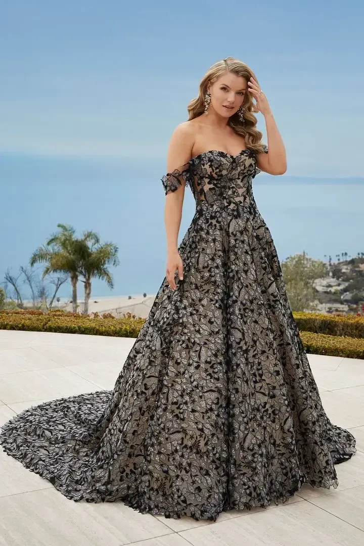 Woman in a black and beige floral gown, off-the-shoulder, train on a patio overlooking the ocean.