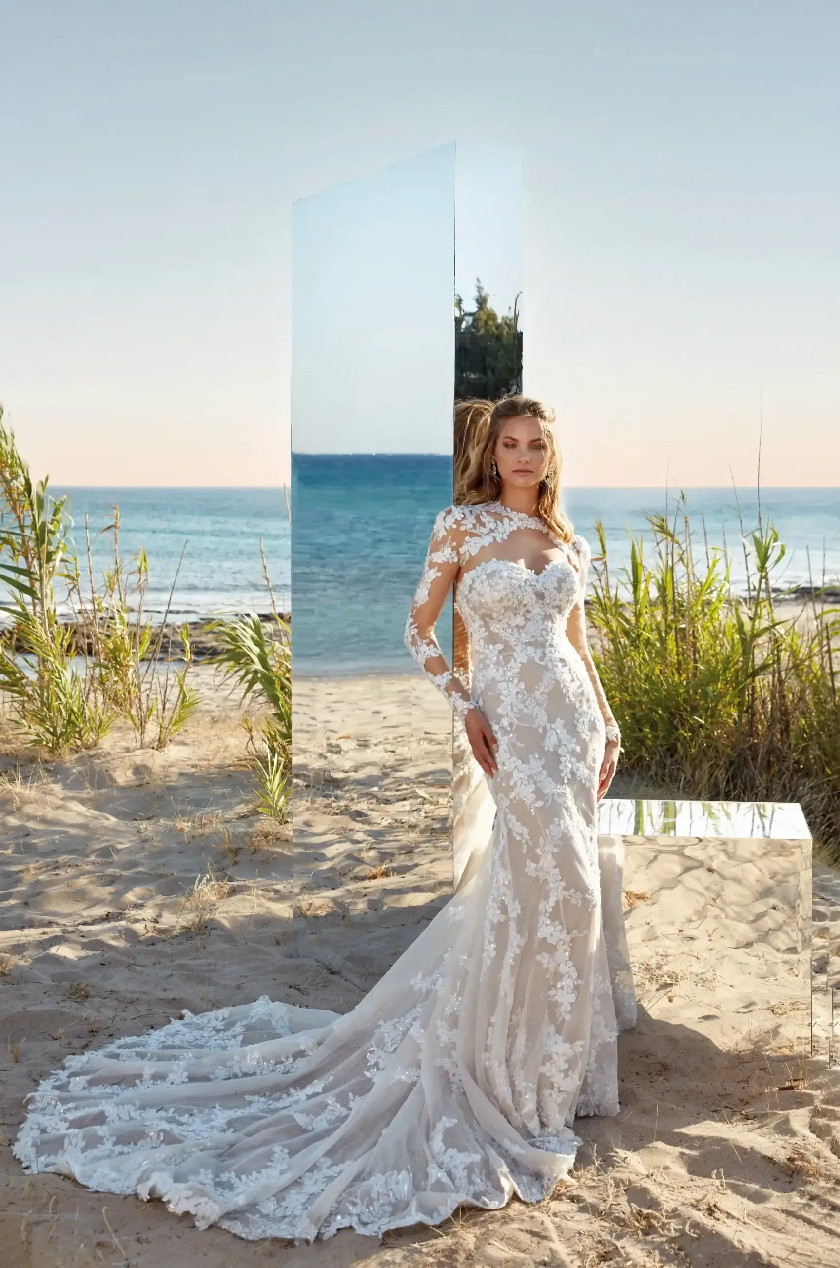 Woman in white lace wedding dress on beach, long train, mirror reflection.