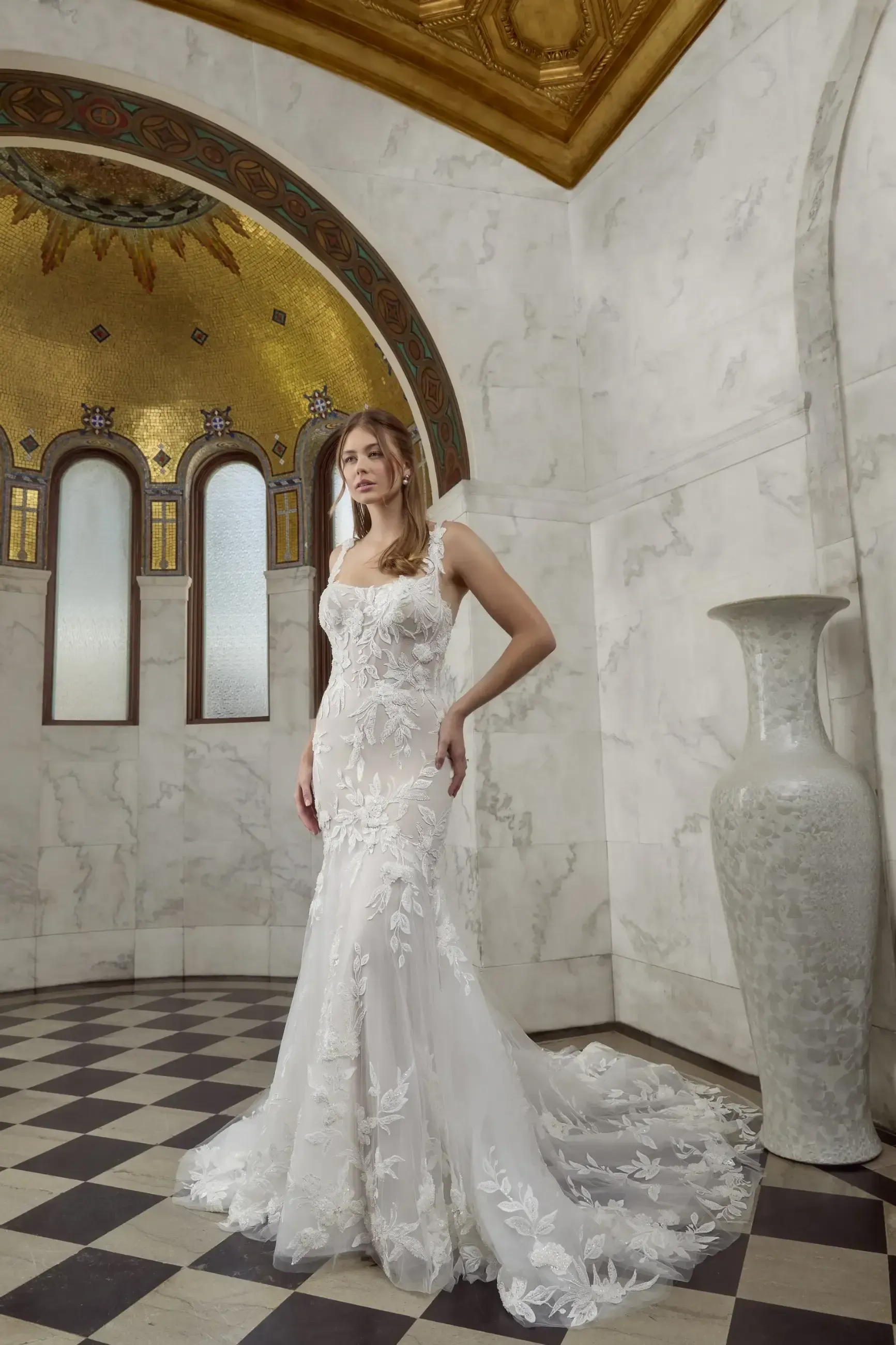 Woman in a white wedding dress stands in a marble-walled room with a golden ceiling.