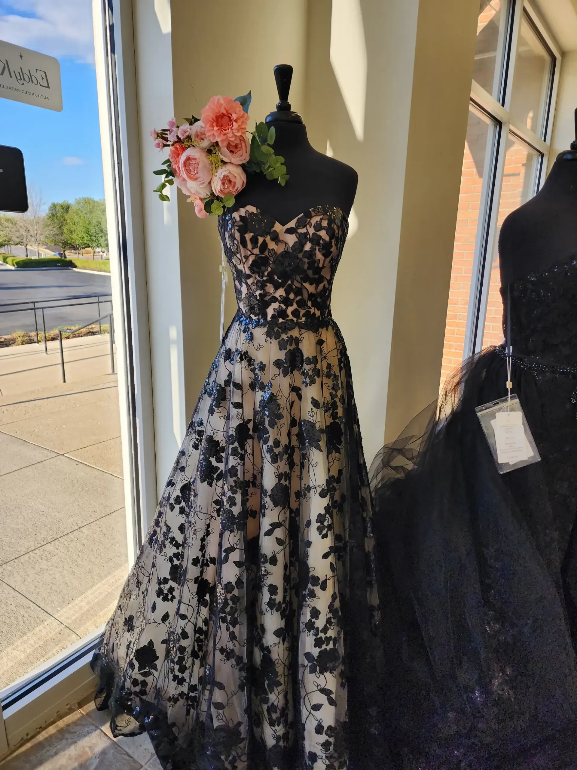 Strapless black floral gown on a mannequin in a window display, with a bouquet.