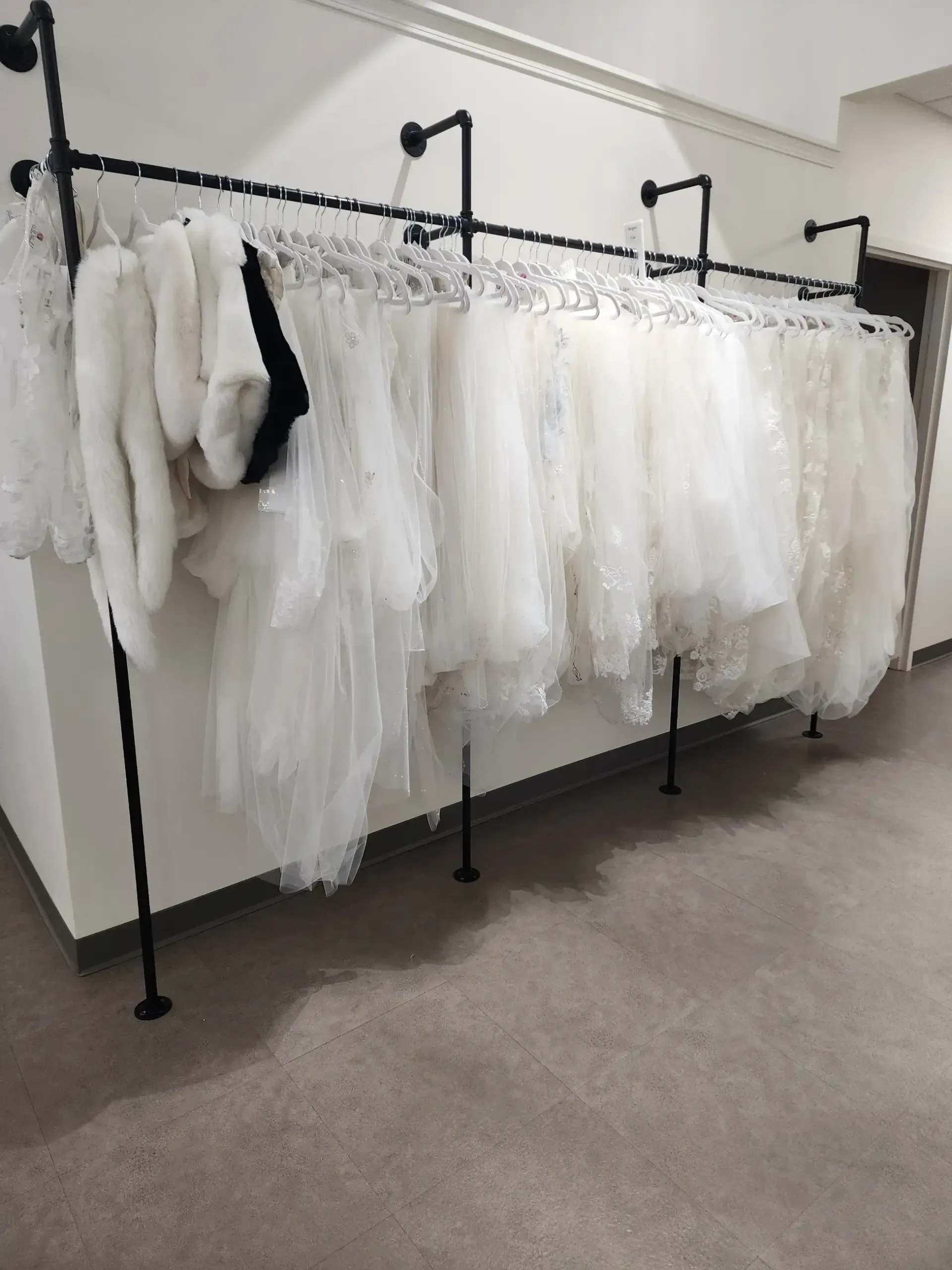 Wedding dresses hanging on a black pipe rack in a bridal shop.