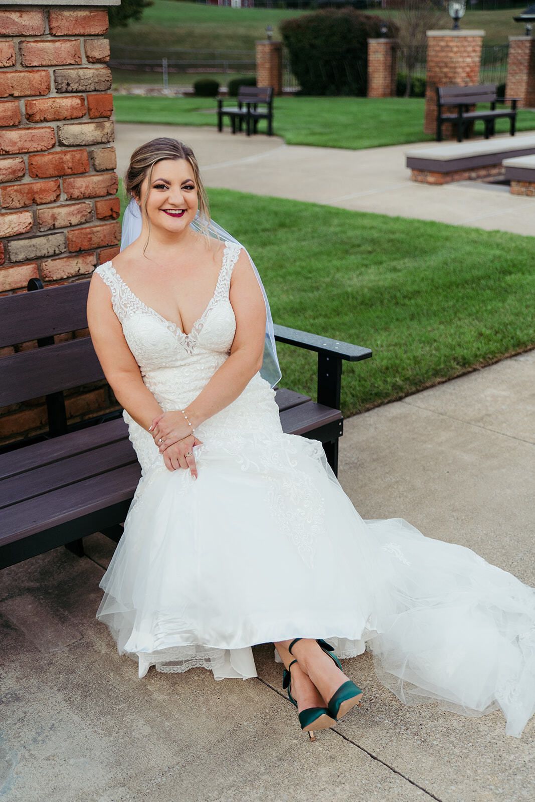 Bride in a white wedding dress and teal heels sits on a bench, smiling outside.
