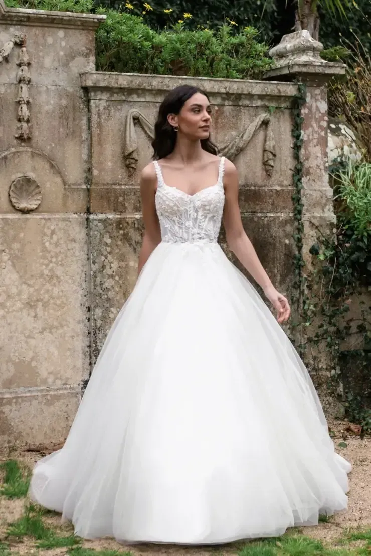 Woman in white wedding dress with floral bodice, posing outdoors.